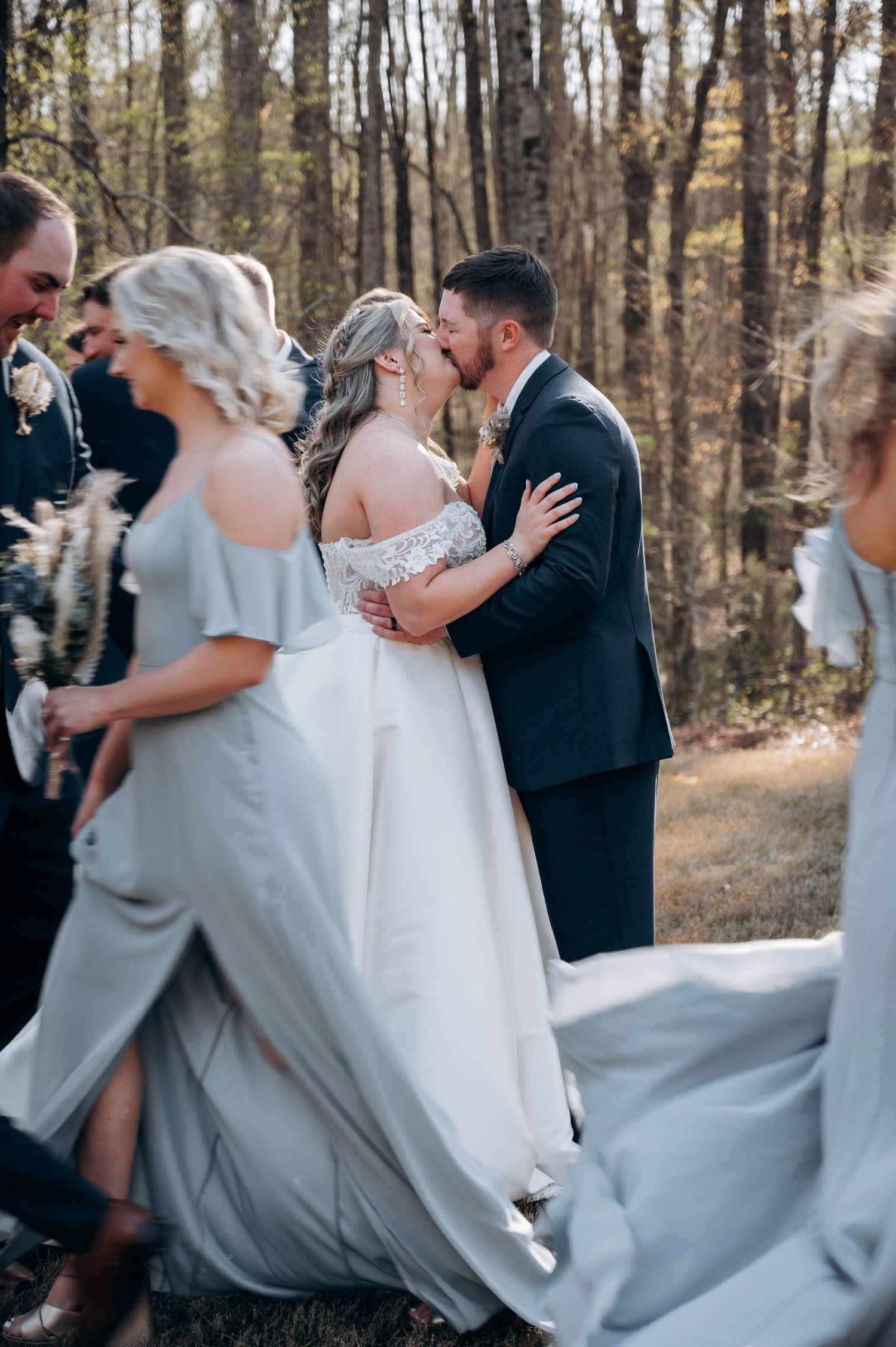 Wedding party celebrates with joyful dancing in an outdoor forest setting.