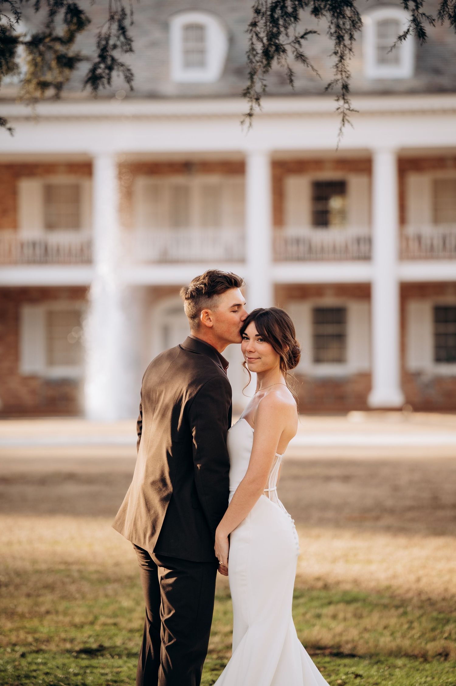 Wedding couple shares intimate moment in front of historic white columned building.