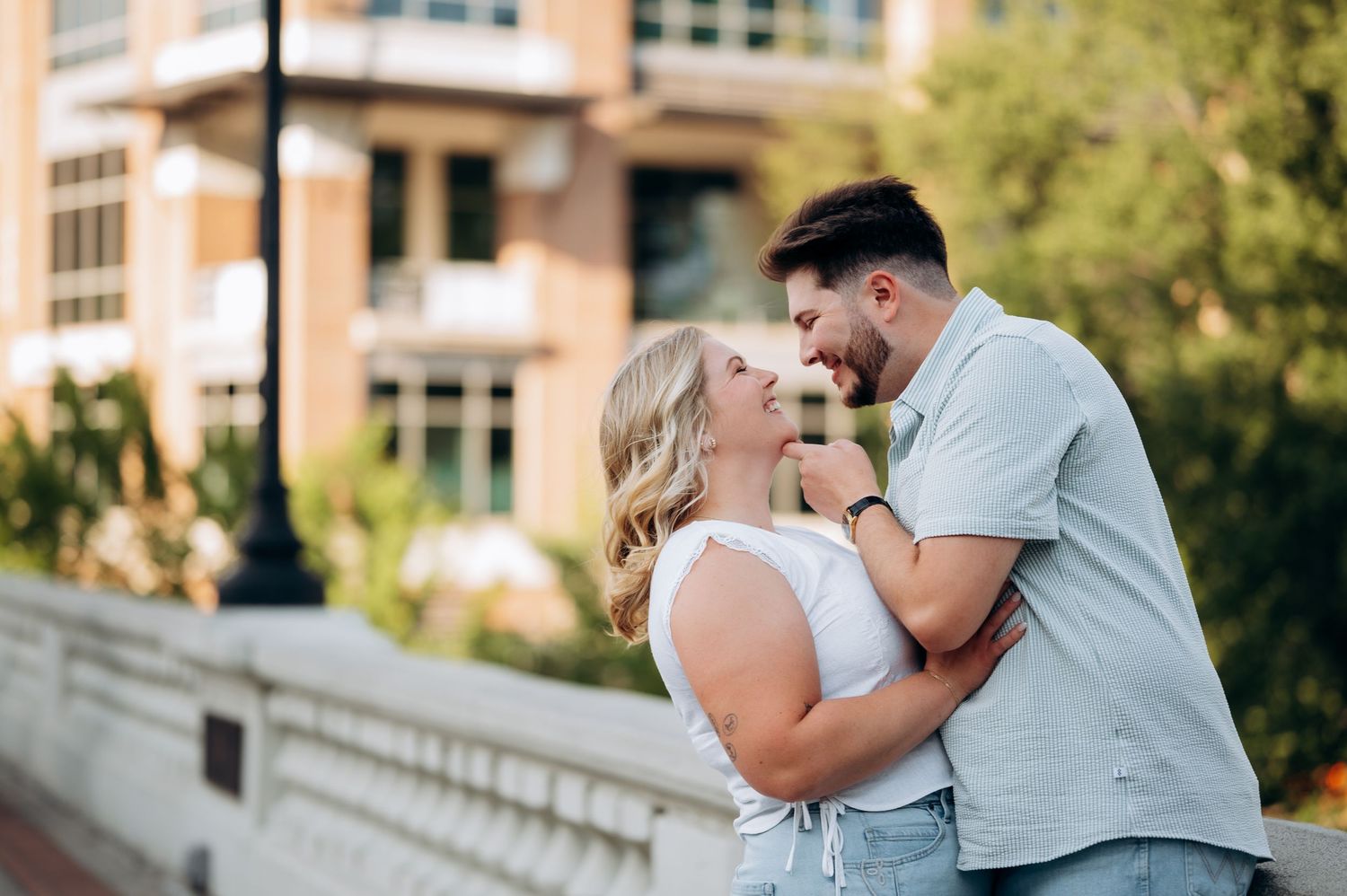 Couple sharing a romantic moment outdoors, embracing and smiling at each other near a white bridge railing.