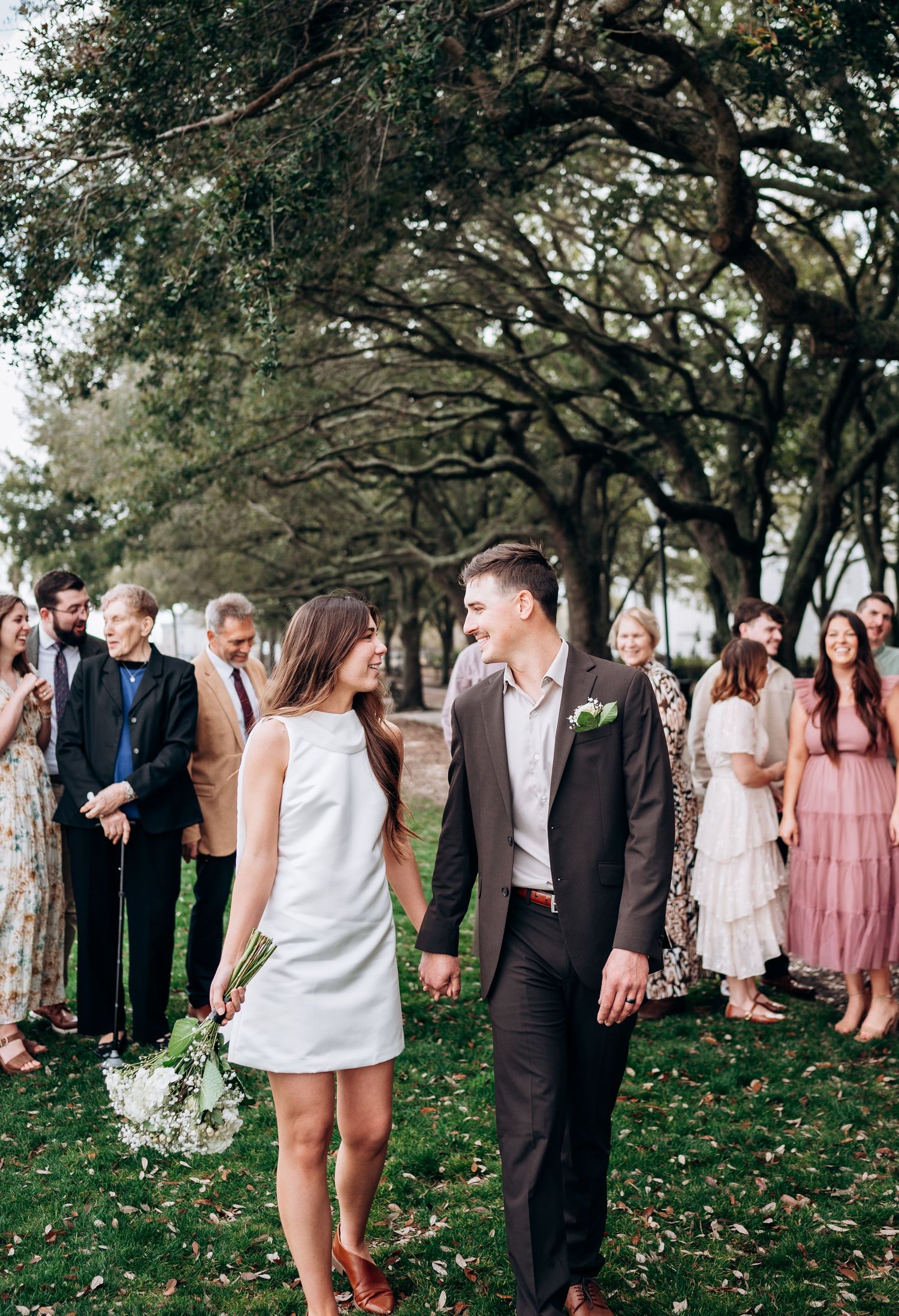 Wedding party gathers under oak trees for outdoor celebration photos.