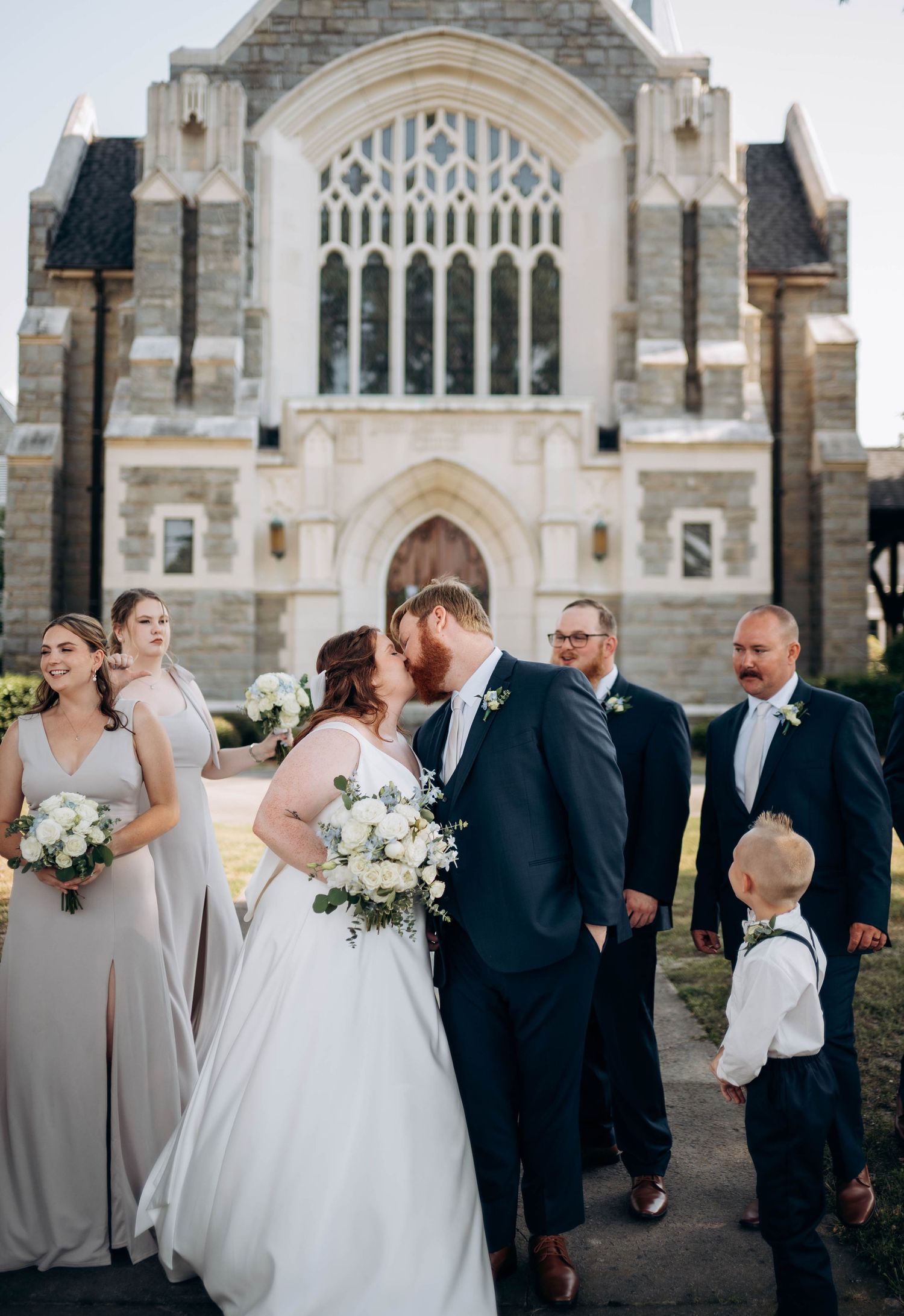 Wedding party gathered outside gothic stone church with ornate architecture.