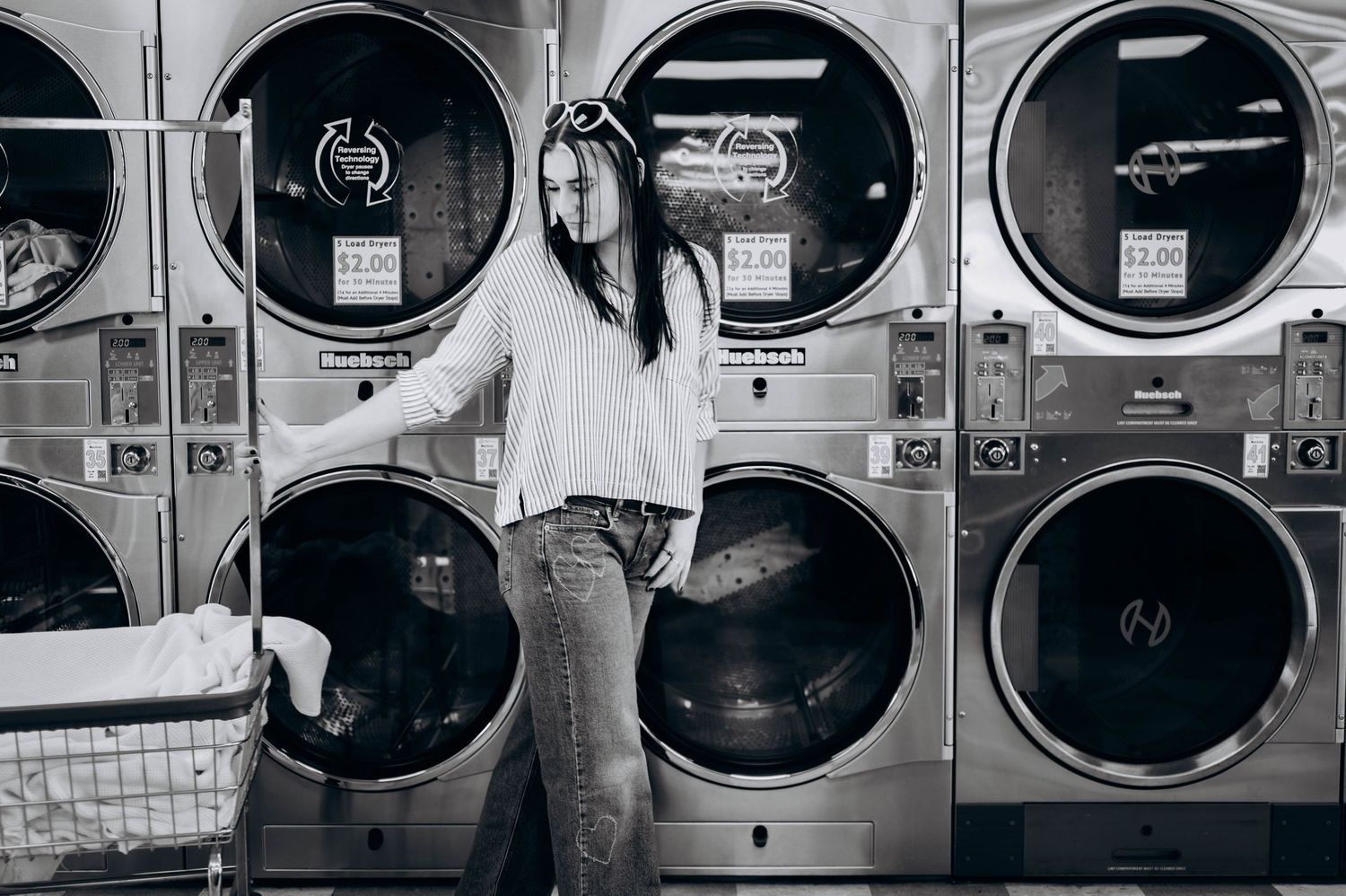 Row of industrial washing machines in black and white at a laundromat.