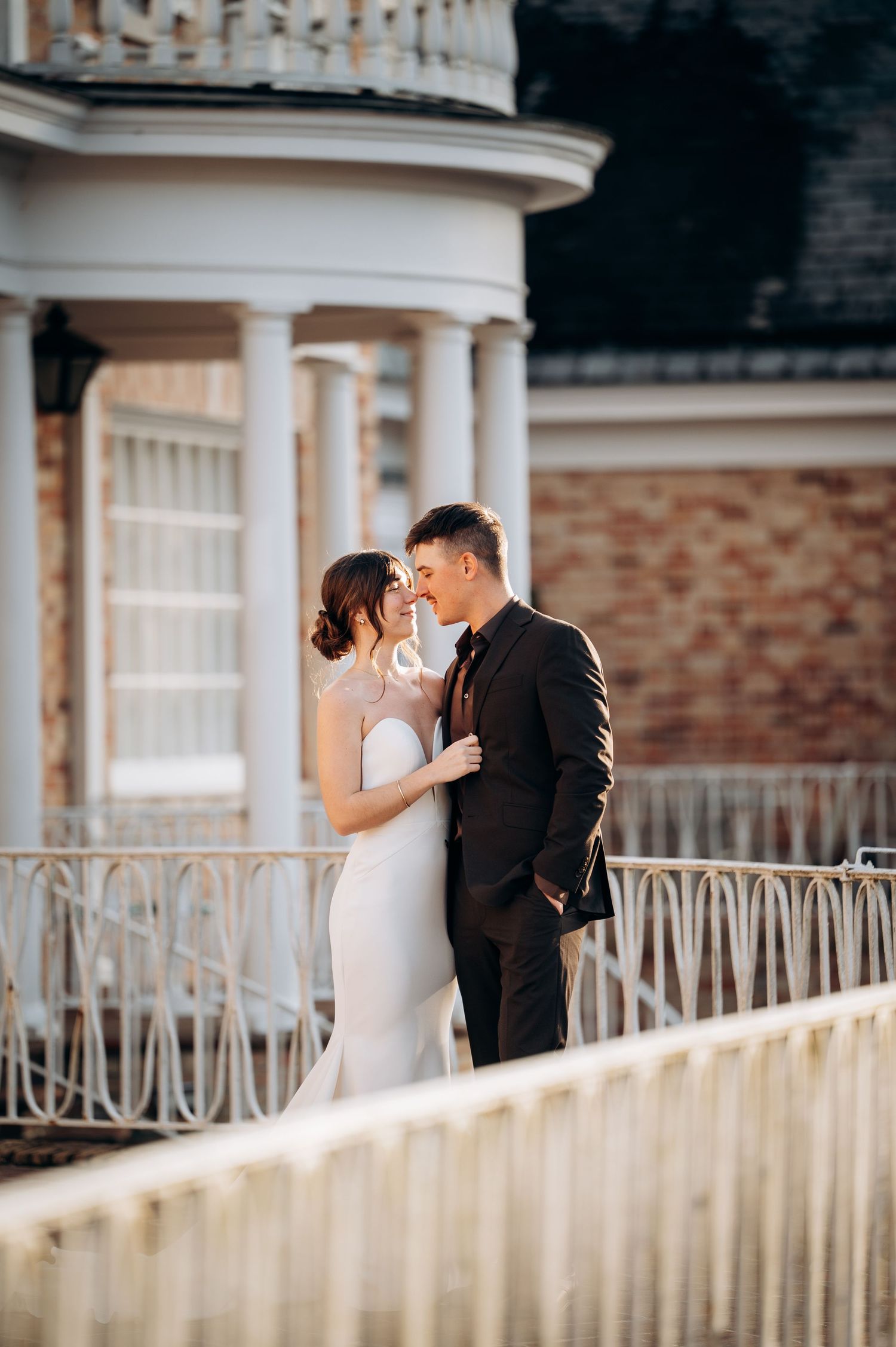 Wedding couple shares intimate moments on a white columned porch with ornate iron railings.