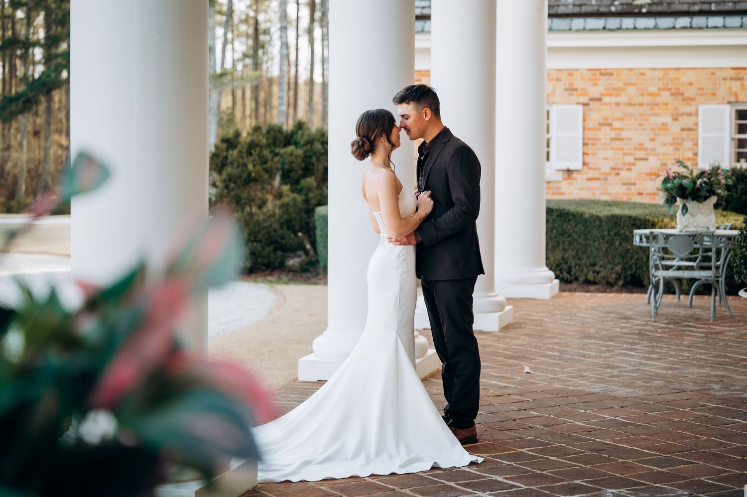 Wedding couple poses on a columned porch of a classic brick building.