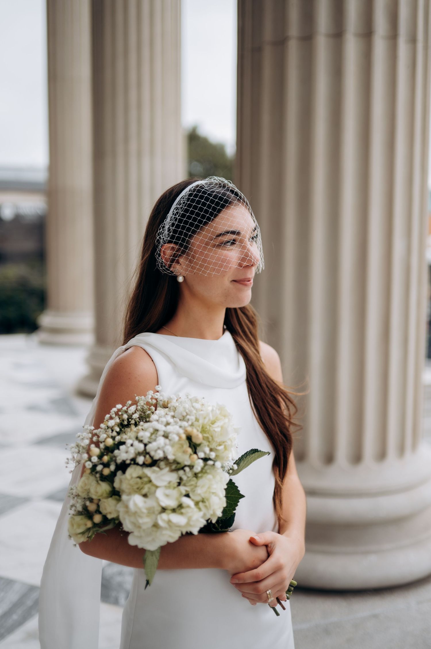 Elegant bridal portrait with white flowers against classic stone columns in natural light.