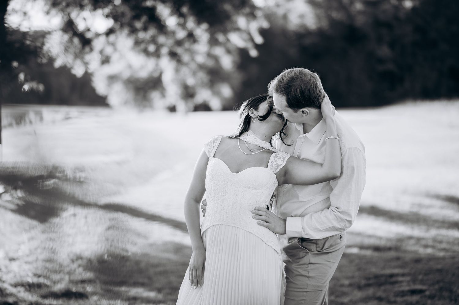 Black and white photo of a pregnant couple sharing a tender moment outdoors, forehead to forehead in a romantic embrace.
