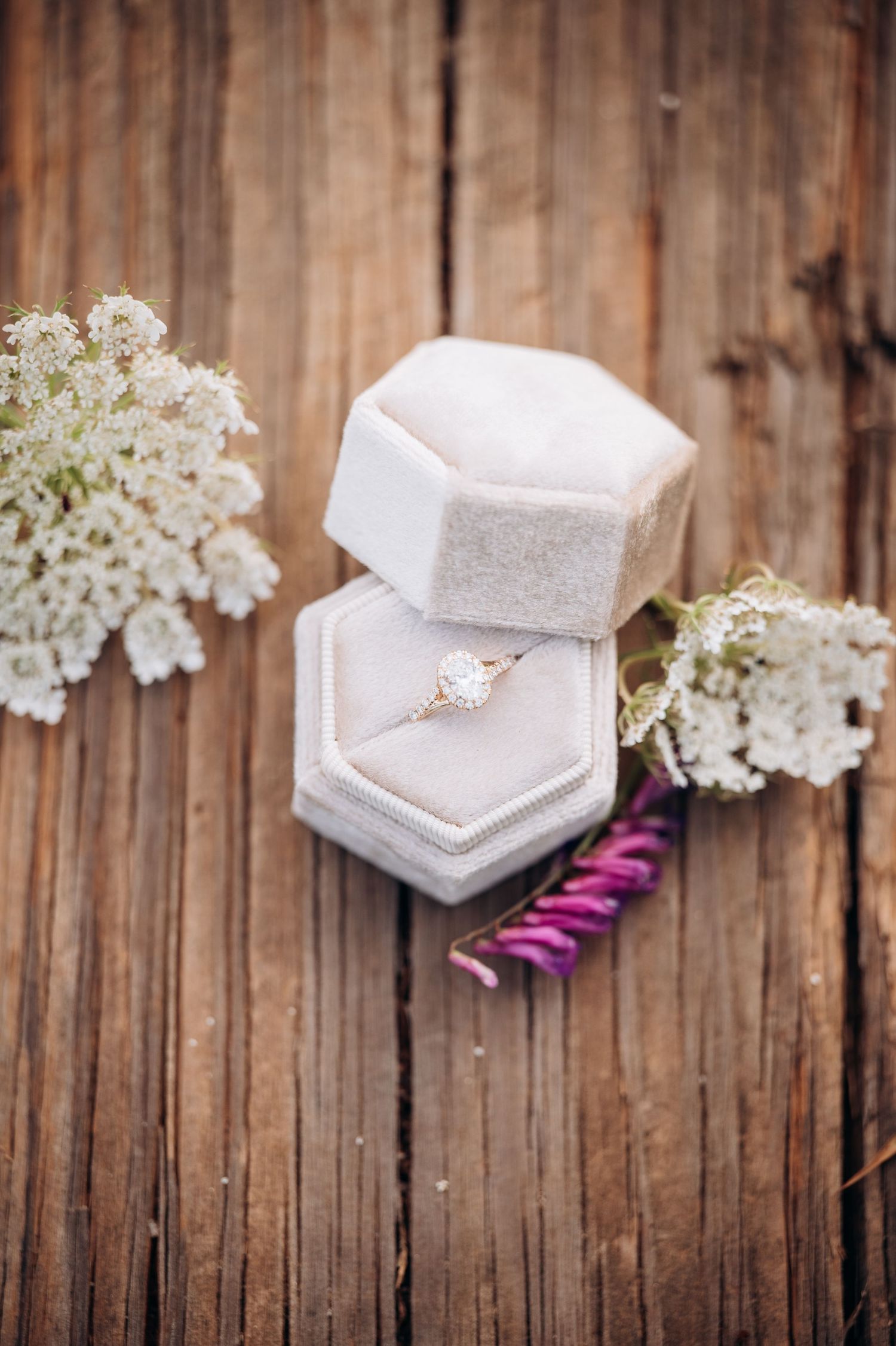 Diamond engagement ring in an elegant hexagonal velvet ring box on rustic wood with white flowers.
