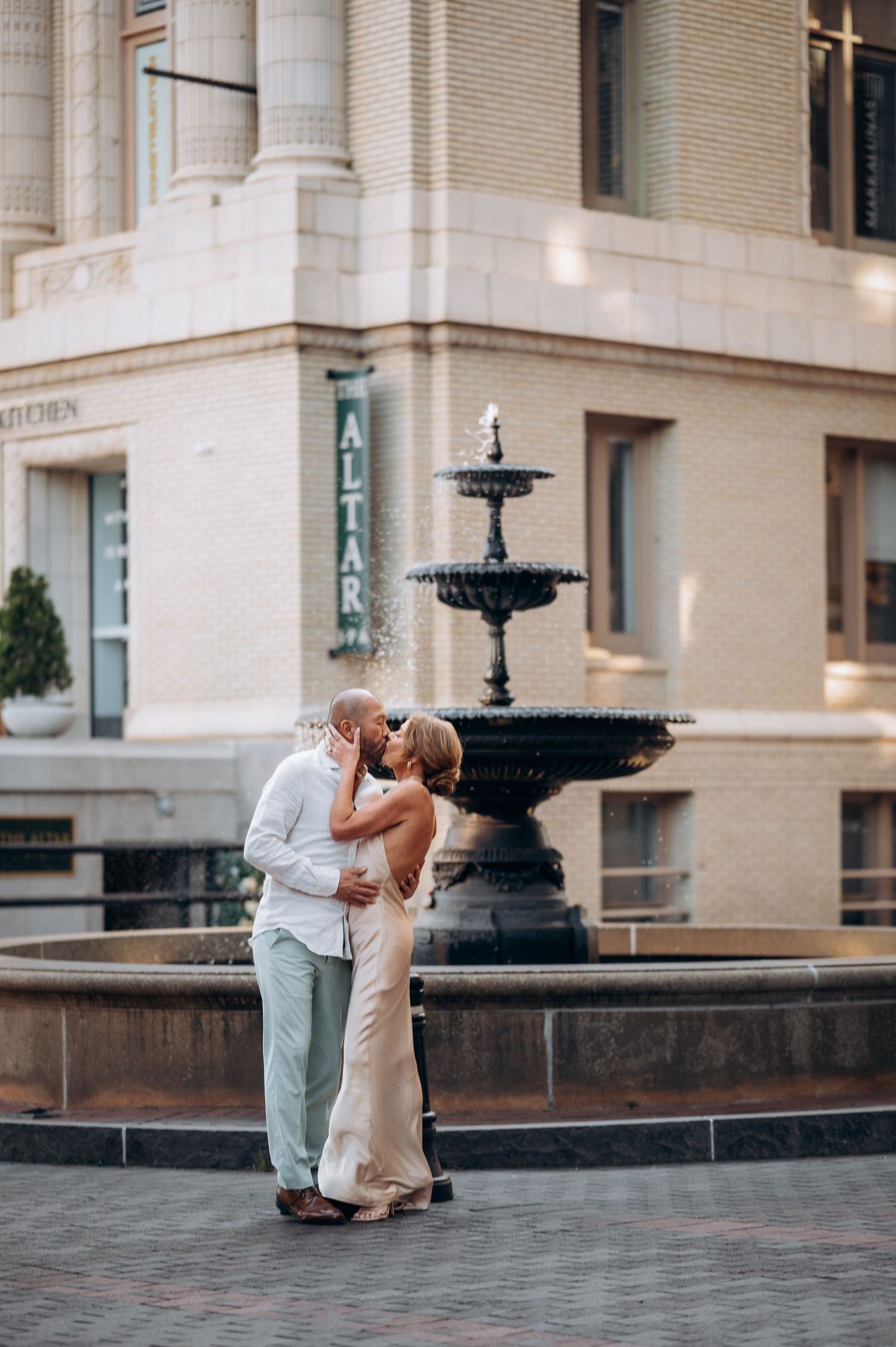 Bride and groom kissing passionately in front of a tiered fountain outside The Altar.
