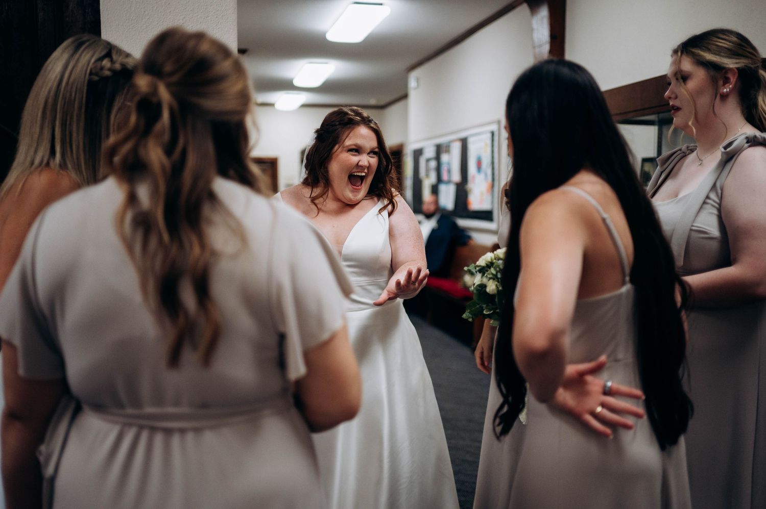Candid wedding party moments captured in indoor venue hallway.