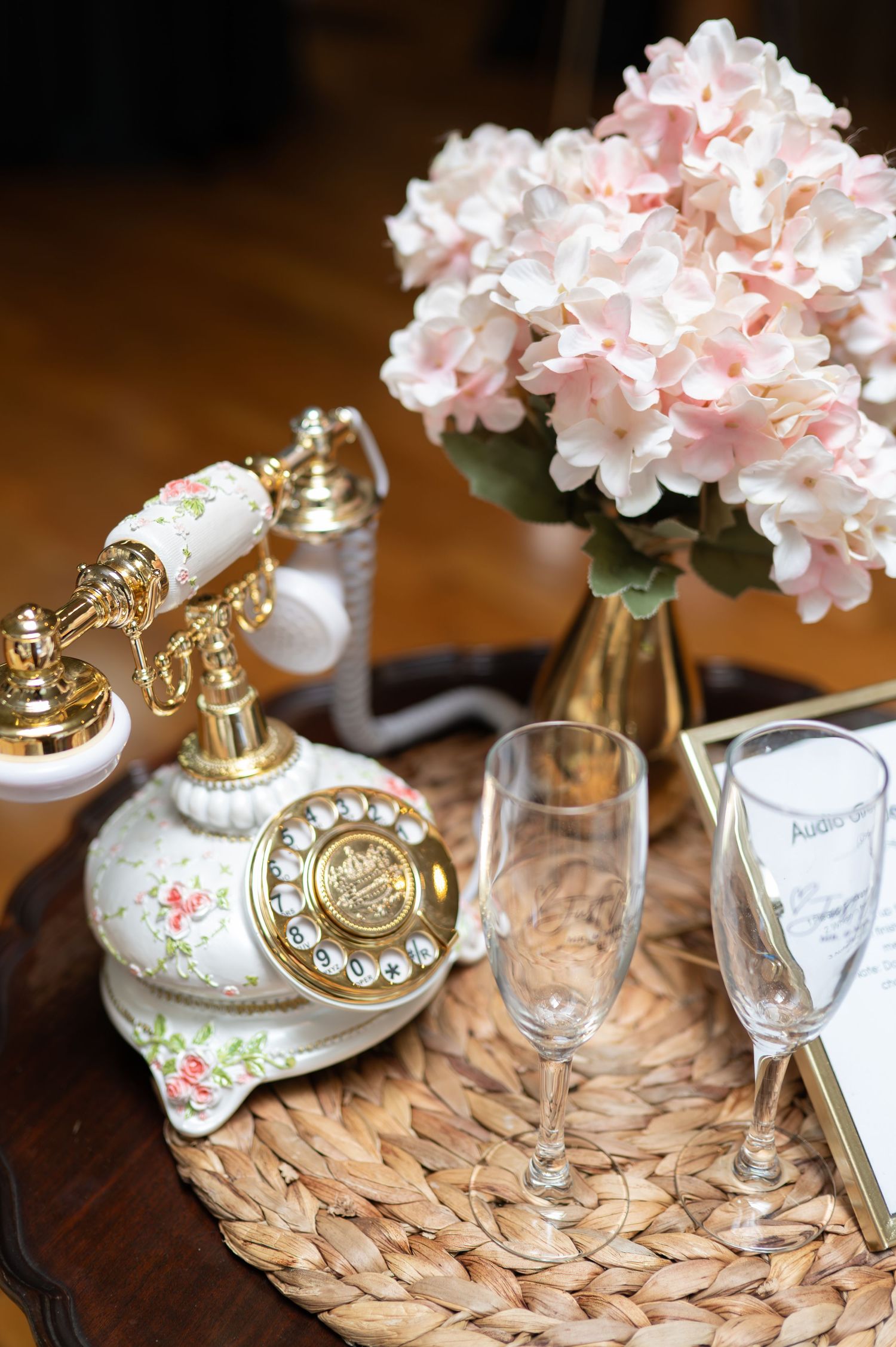 Vintage rotary telephone with pink floral decorations and hydrangeas arranged on woven placemats.