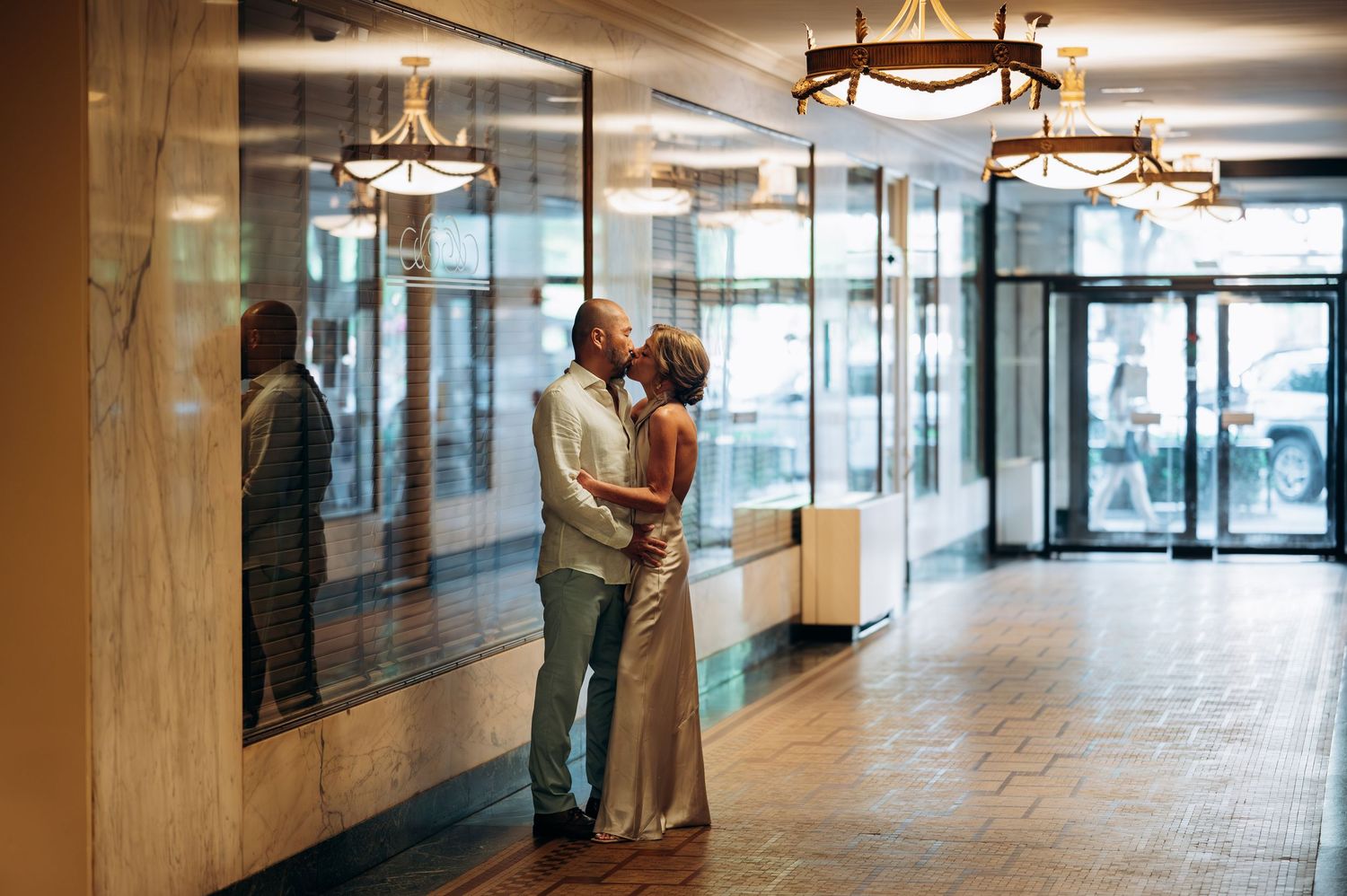 Couple sharing a romantic kiss in an elegant hotel lobby with warm lighting and marble walls.