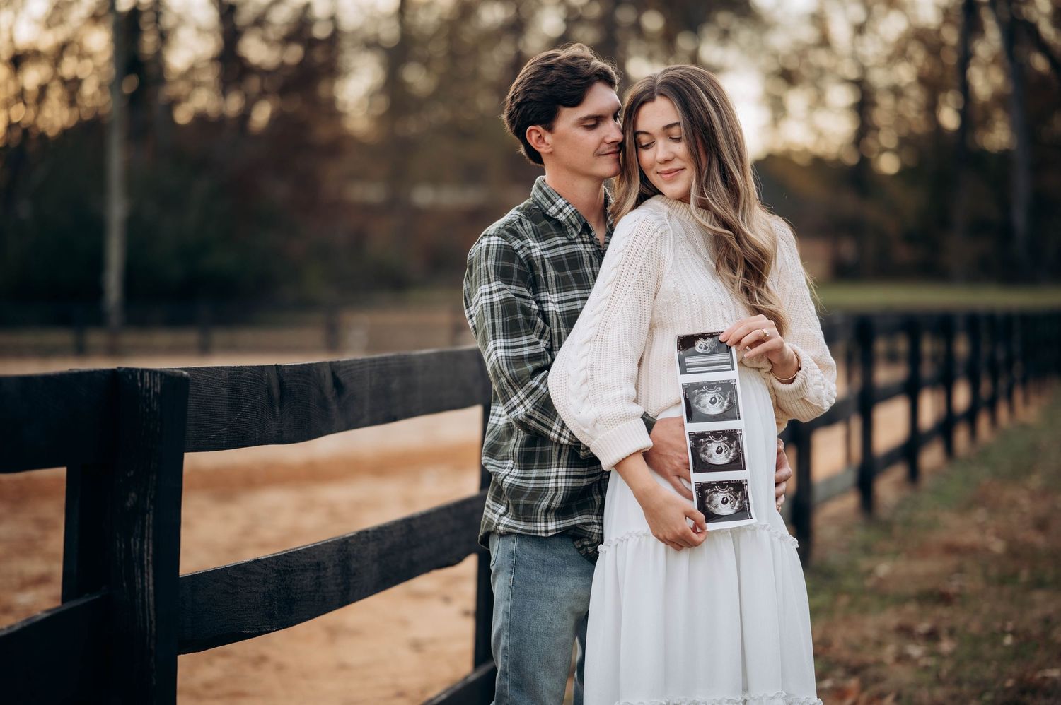 A couple embraces by a wooden fence during their autumn pregnancy announcement photoshoot.