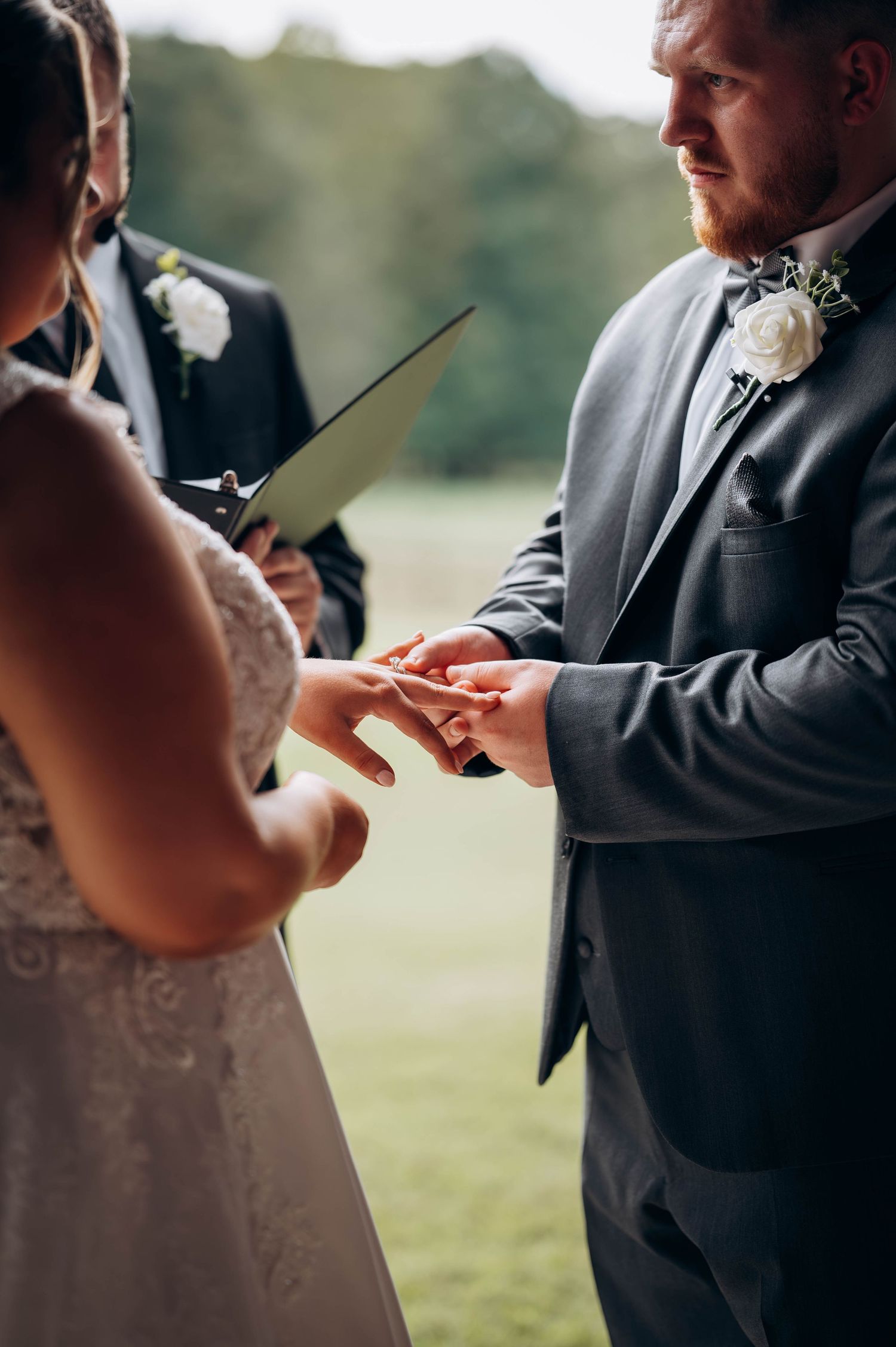 Close-up of hands exchanging vows during an outdoor wedding ceremony.