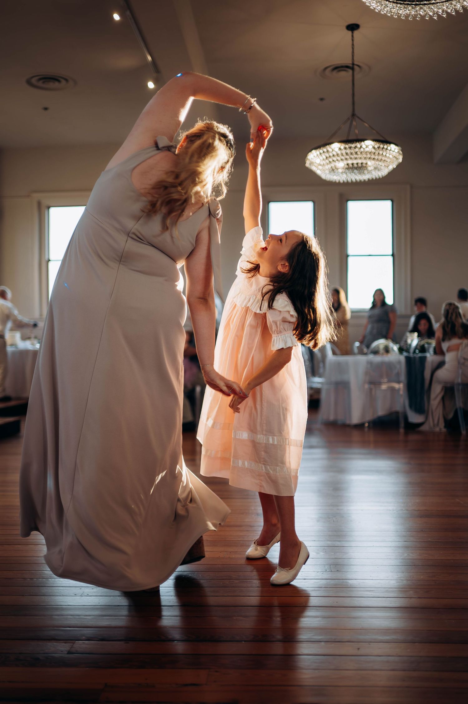 Sweet moment of dancing between woman in formal dress and young girl in white dress.