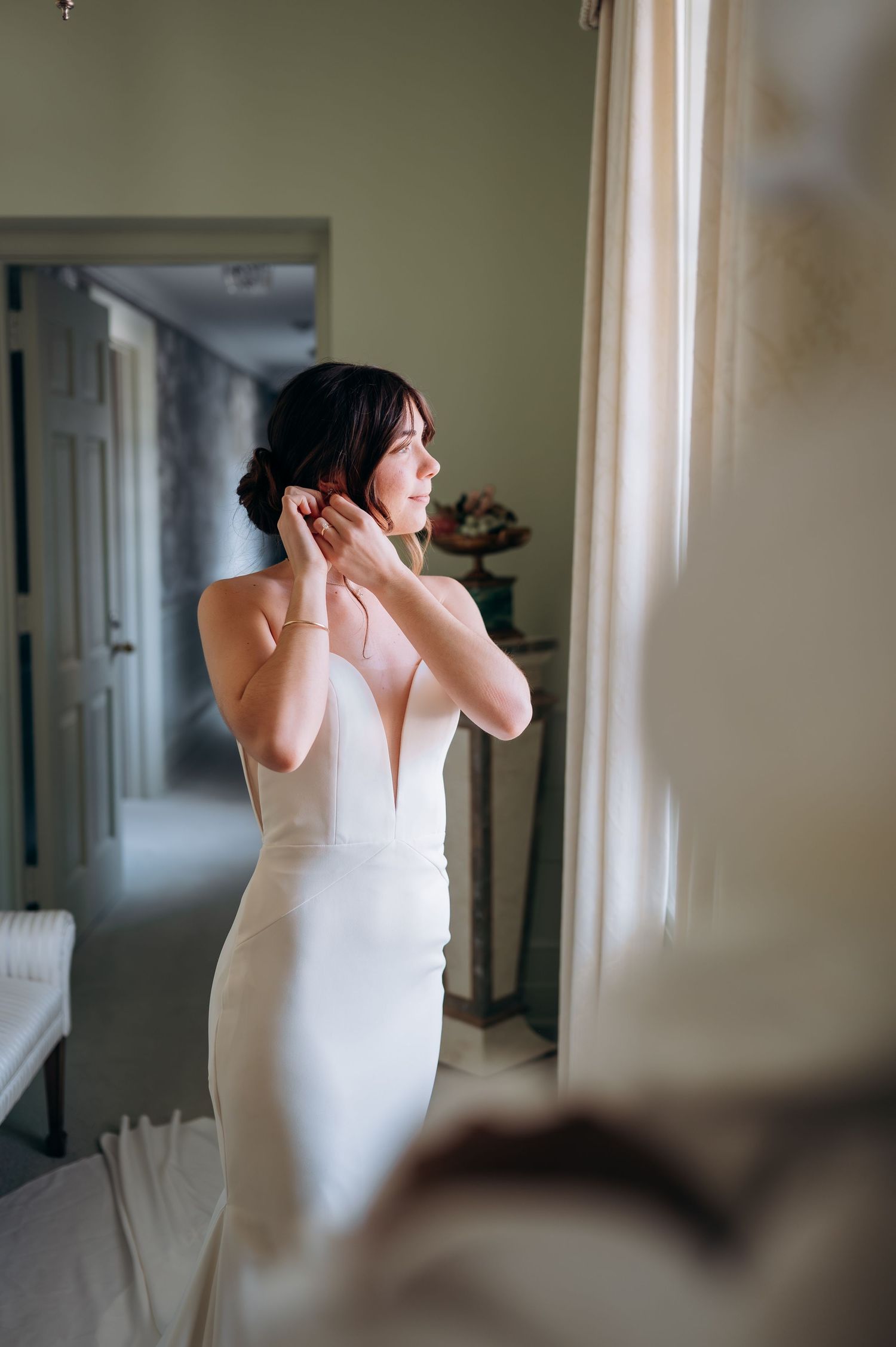 Bride getting ready in a white dress against a sage green wall.