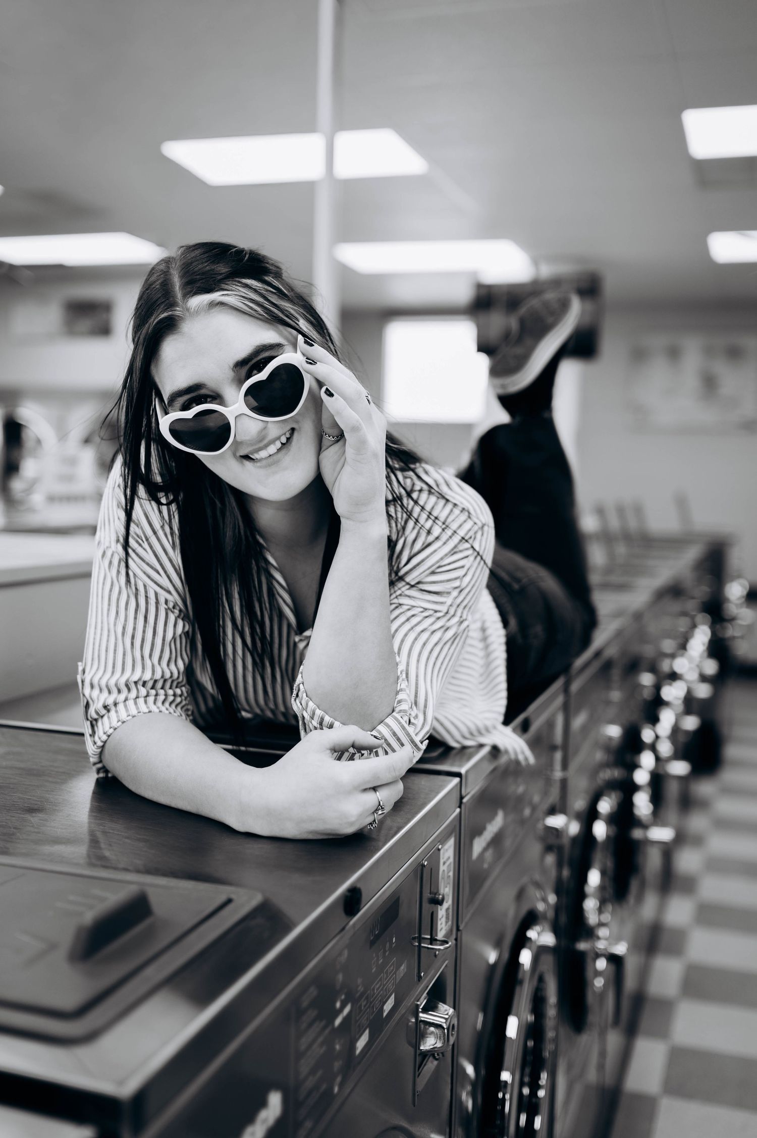 Black and white photo of person in striped shirt lying on table at a diner counter with sunglasses.