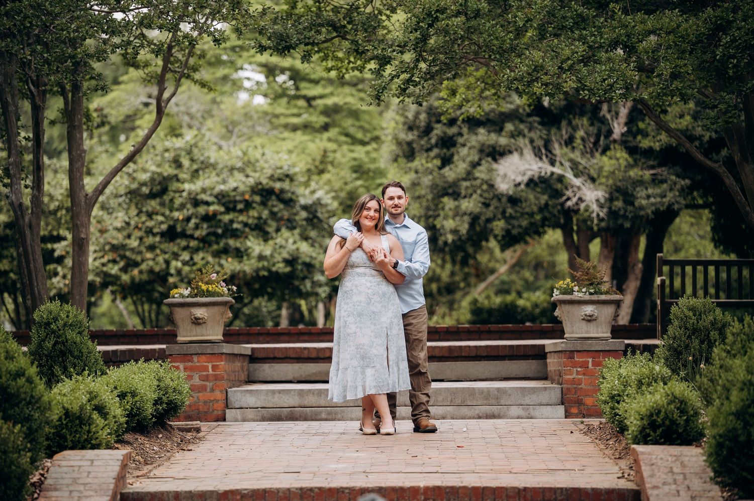 Happy couple posing together on brick steps surrounded by lush greenery in a formal garden.