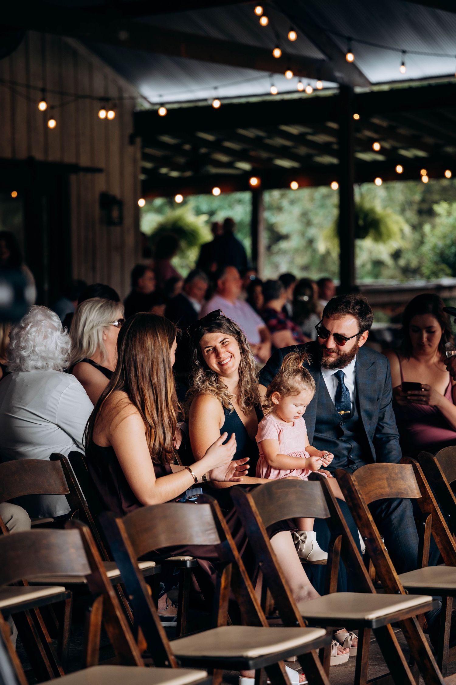 Wedding reception venue with string lights and wooden chairs filled with guests.