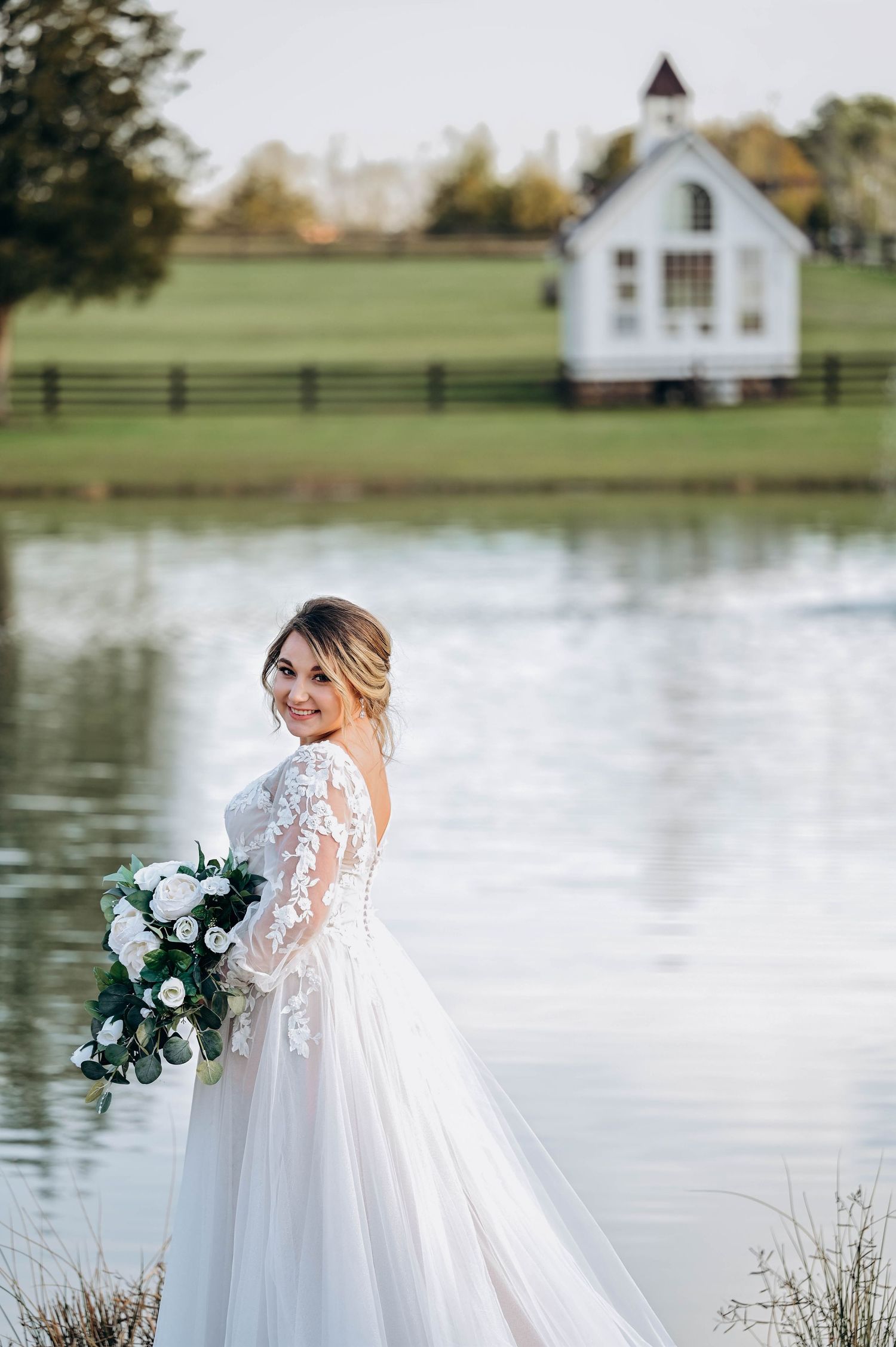 Ethereal bridal photos by lakeside with white chapel in background.