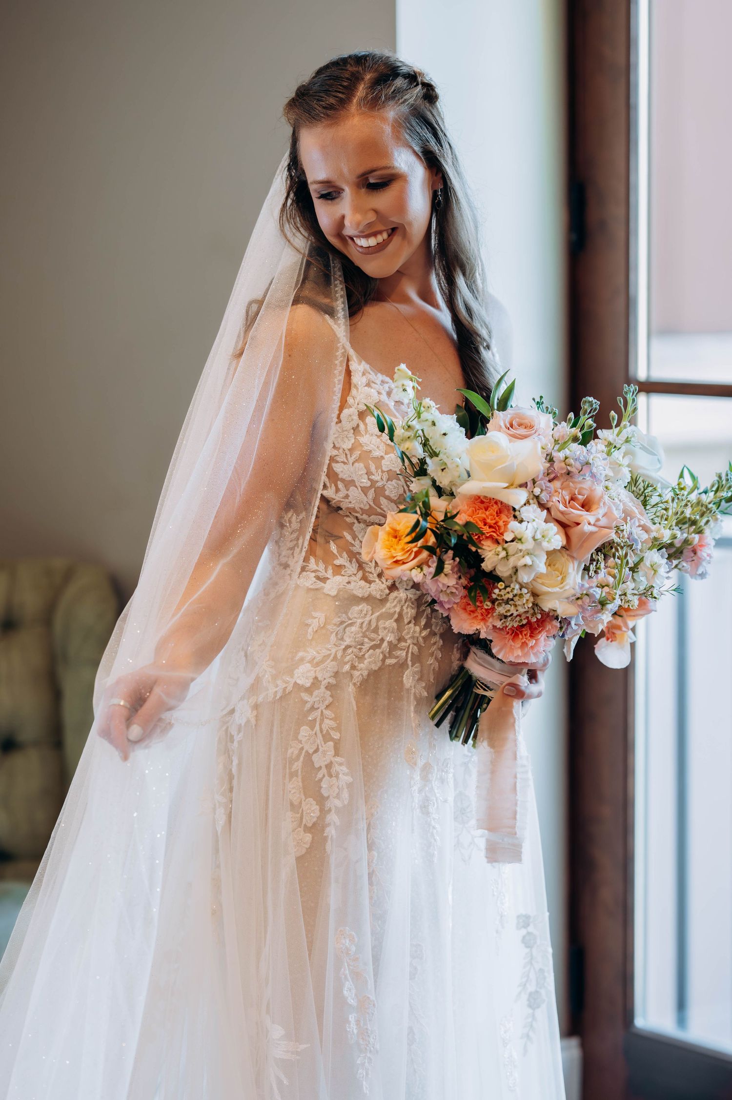 Joyful bridal portrait with peach and cream floral bouquet in natural window light.
