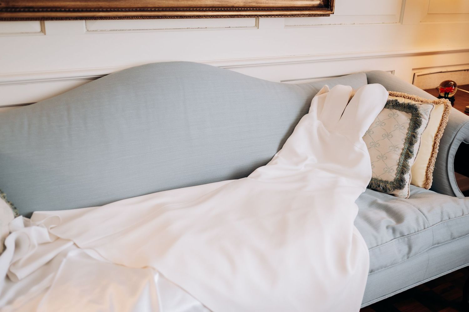A cozy bed with a light blue upholstered headboard, white bedding, and decorative pillows in a bright room.