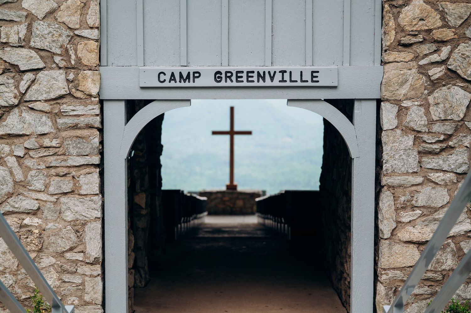 Stone archway entrance to Camp Greenville with a wooden cross visible through the tunnel opening.