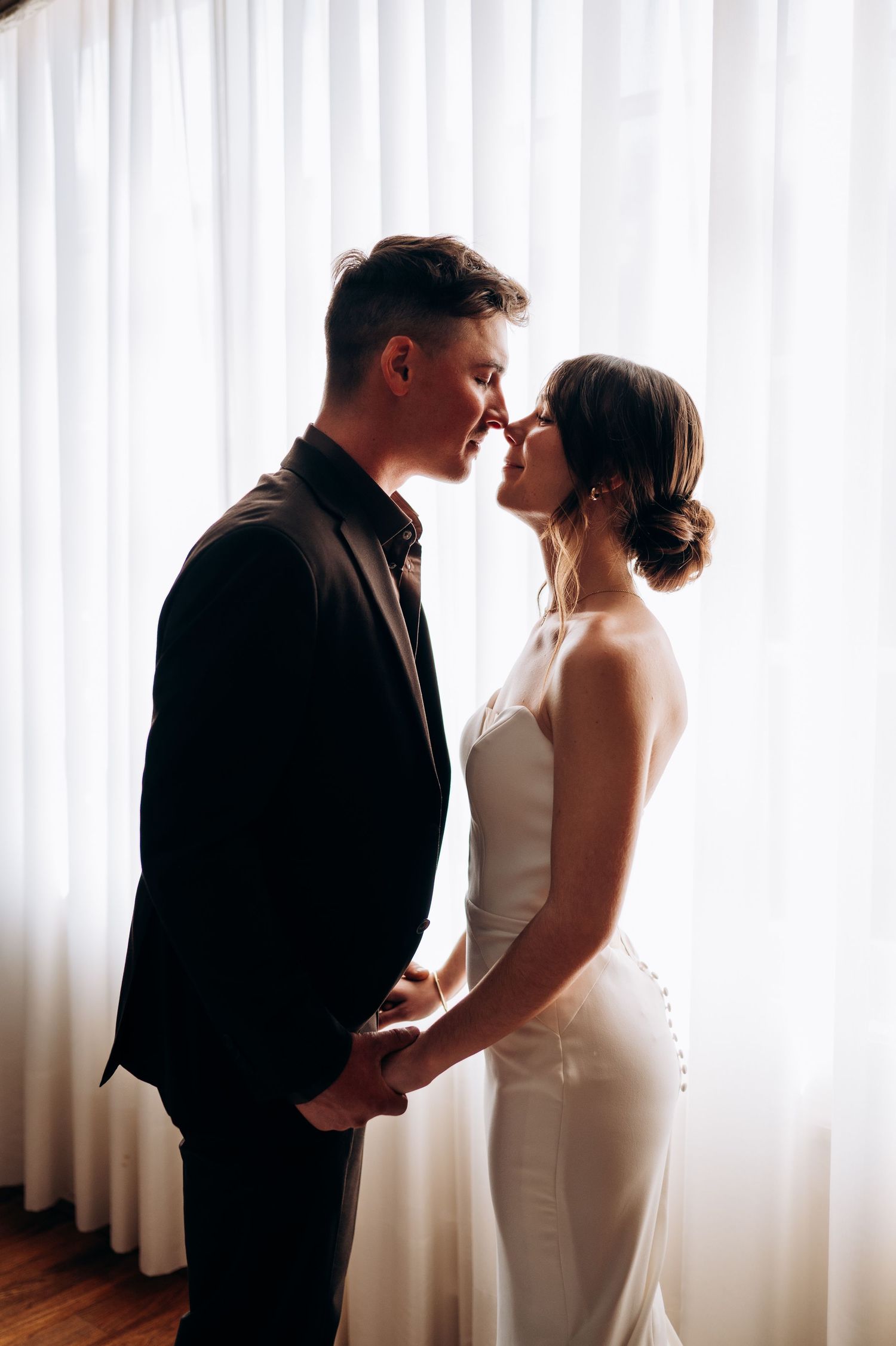 A romantic silhouette of a couple sharing a private moment by sheer white curtains.