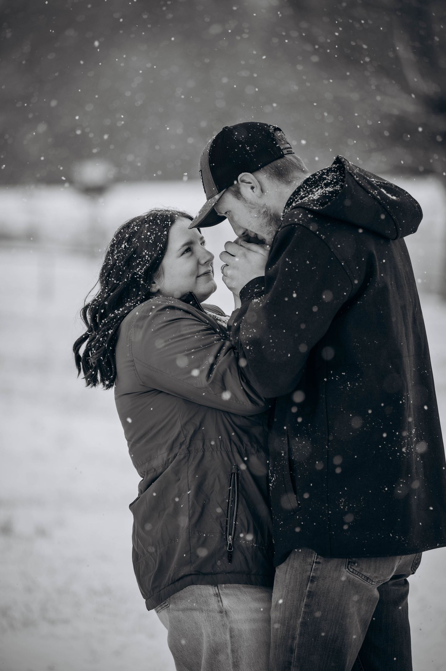 A romantic winter scene shows two people embracing as snow falls around them in black and white.
