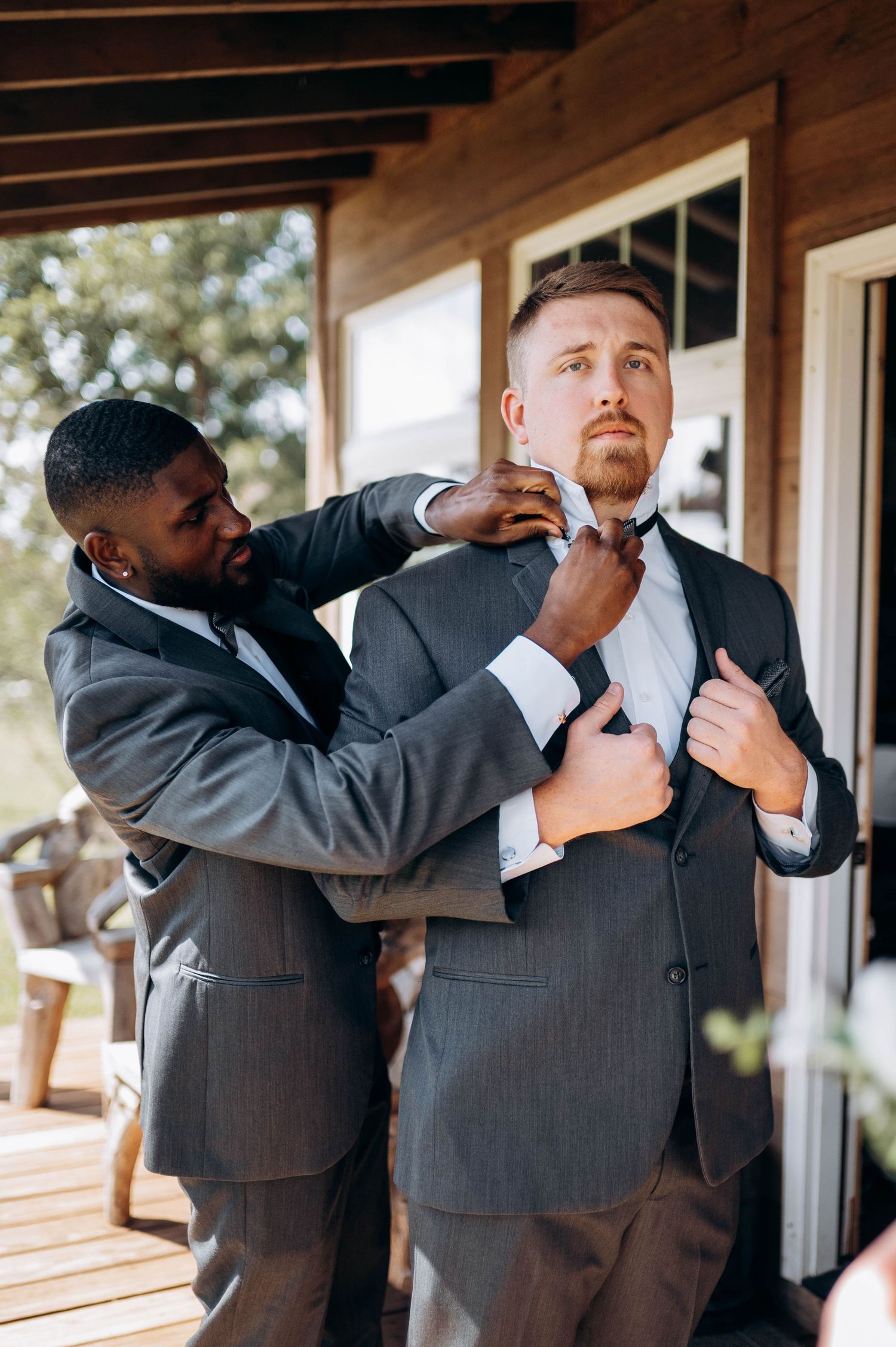 Groomsmen in gray suits helping each other adjust their ties and formal attire.