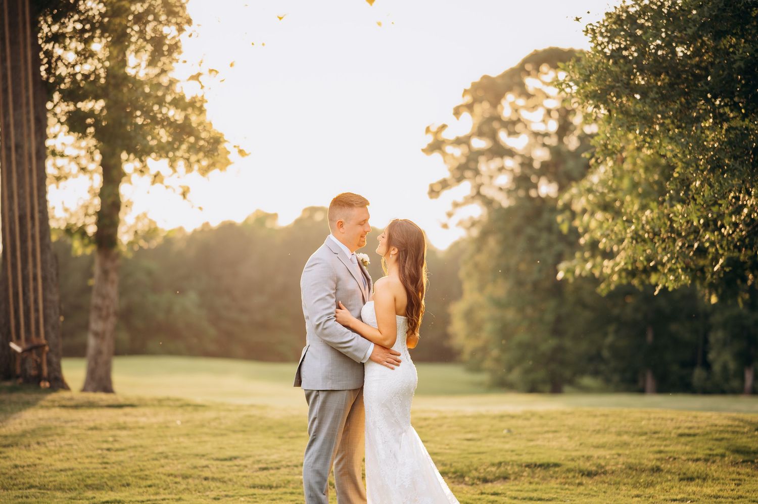 Bride and groom sharing a romantic kiss at golden hour in a lush green outdoor wedding venue.
