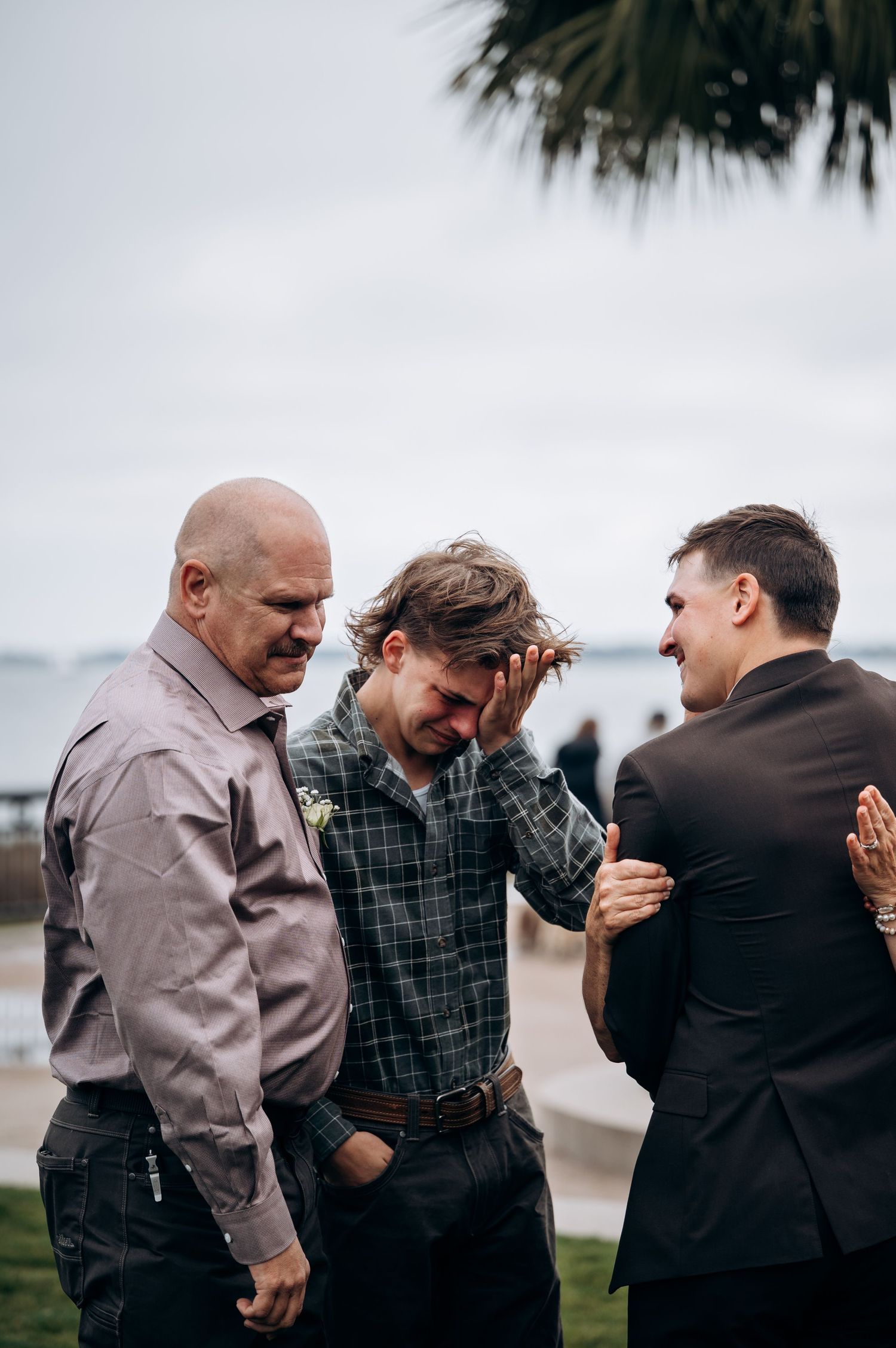 Group of men share emotional embraces during outdoor gathering.
