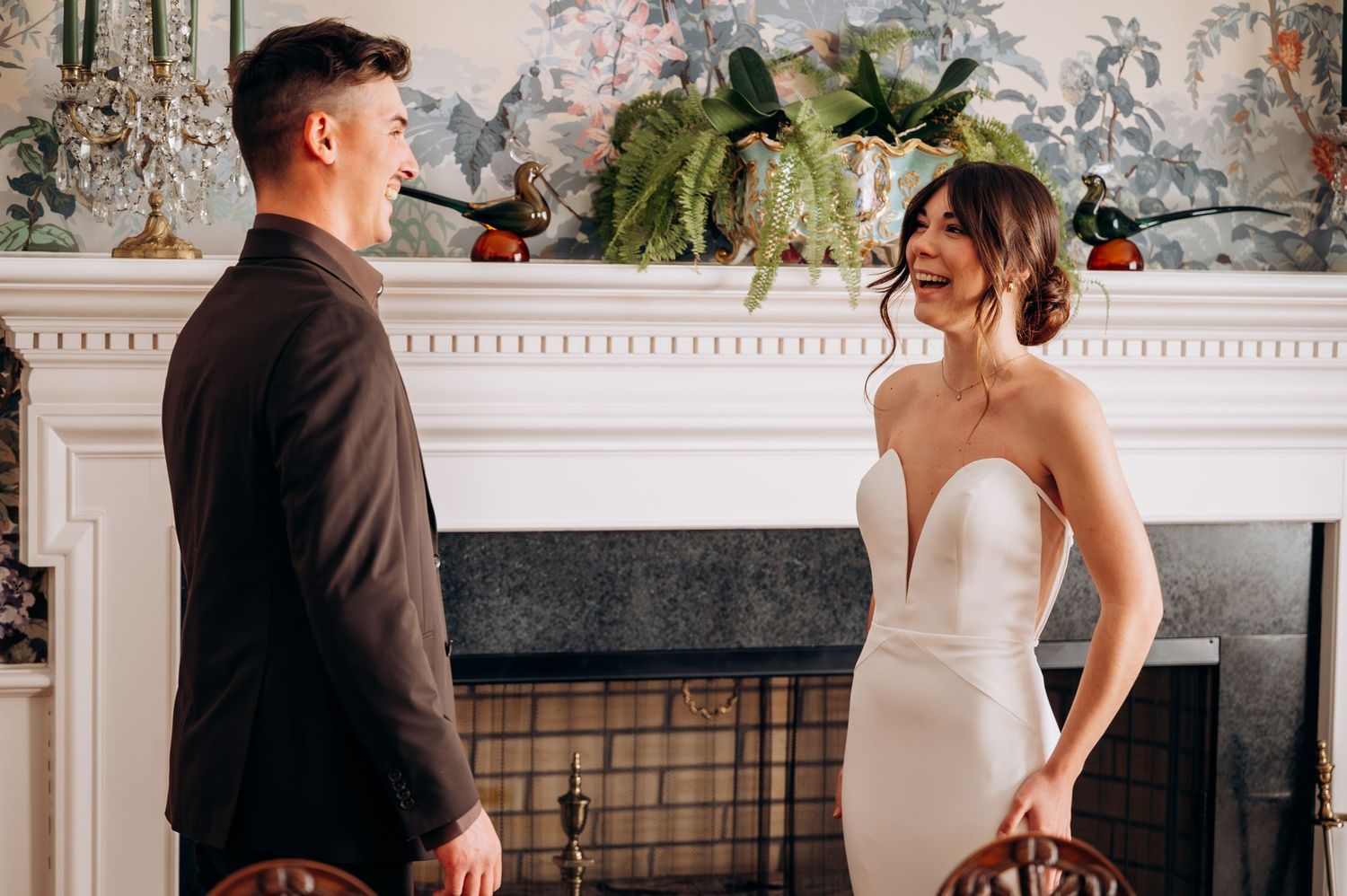 Couple sharing a romantic moment in elegant room with fireplace, woman in strapless white gown, man in dark suit.