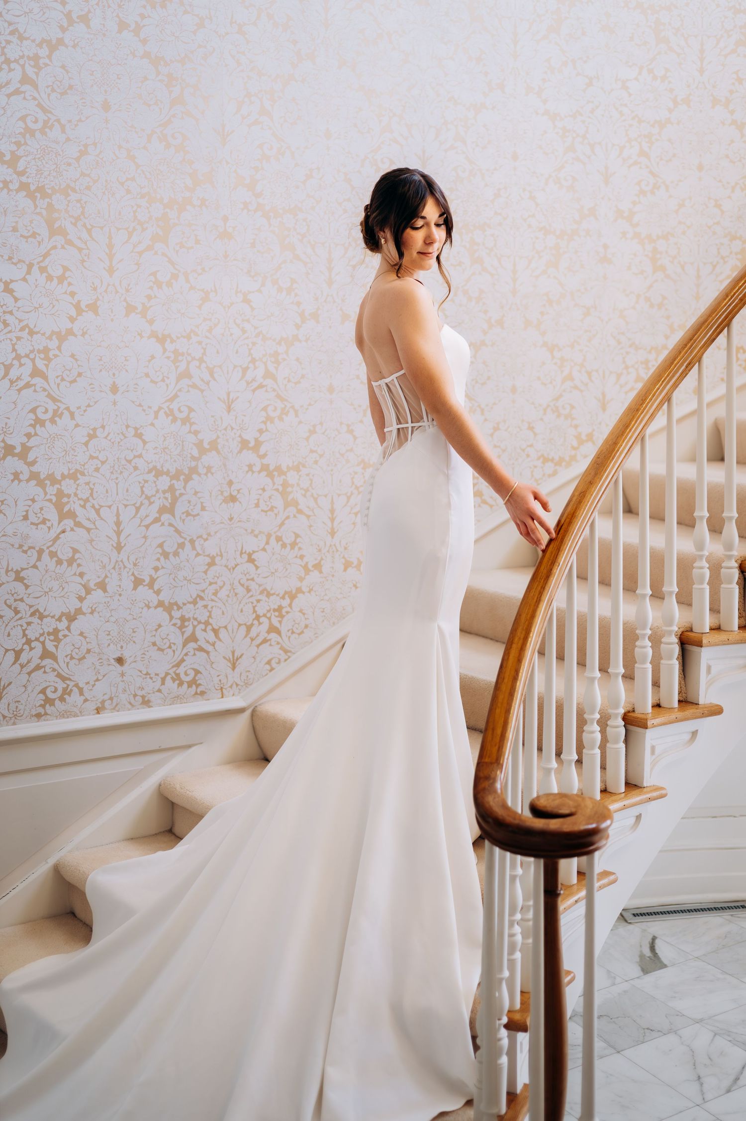 Bride in a strapless mermaid wedding gown with corset back stands on a grand staircase.