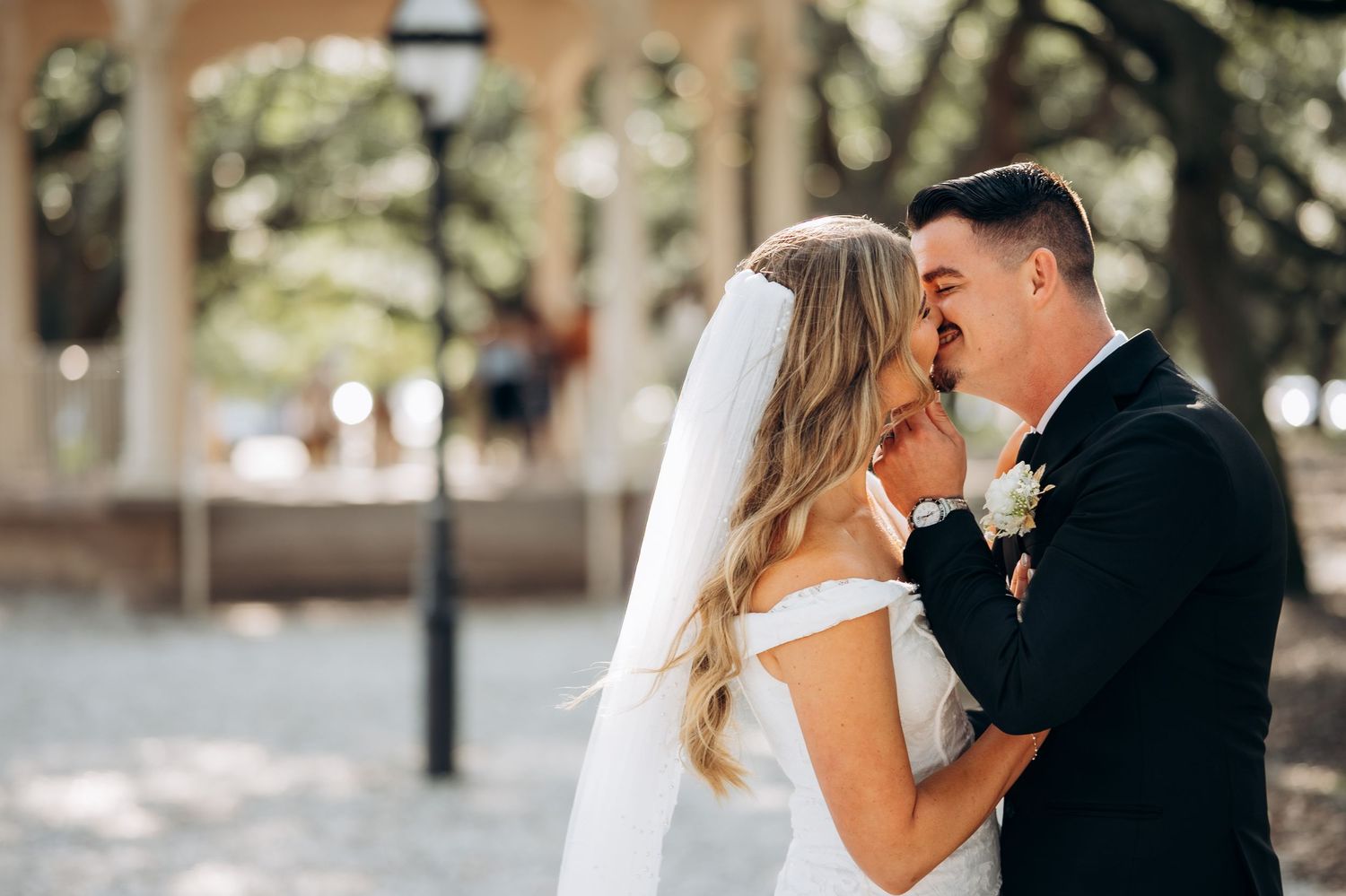 Bride and groom share a romantic kiss outdoors, with the bride in a white gown and veil at their wedding.
