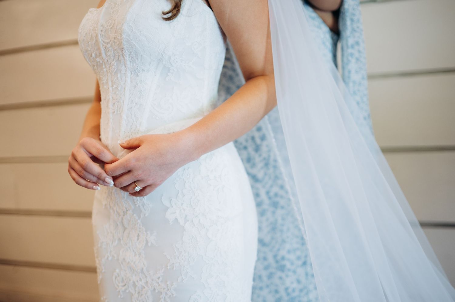 Close-up of bride in fitted lace wedding dress being buttoned by bridesmaid before the ceremony.