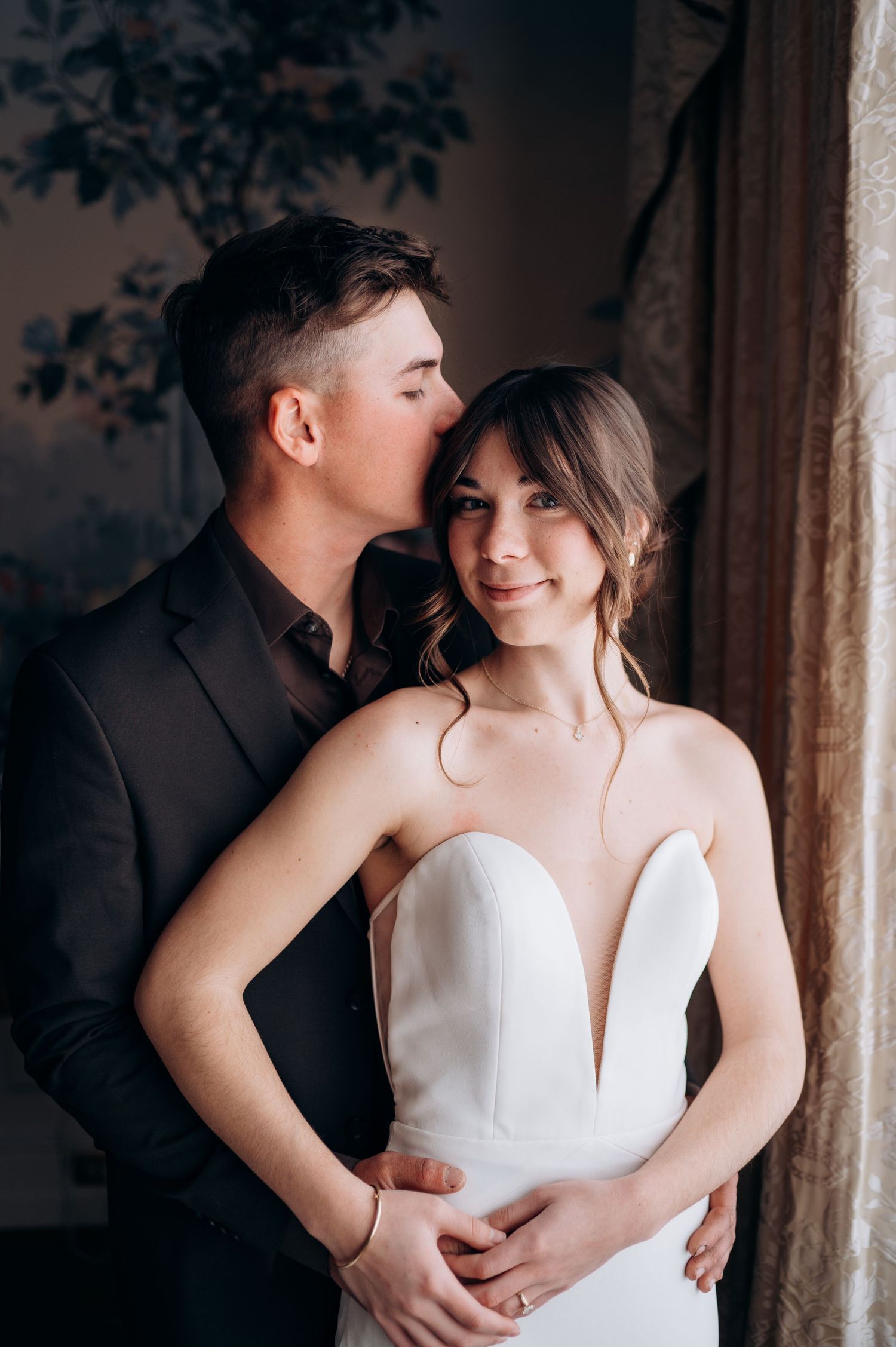 Tender embrace captured in moody lighting with bride in elegant white gown.