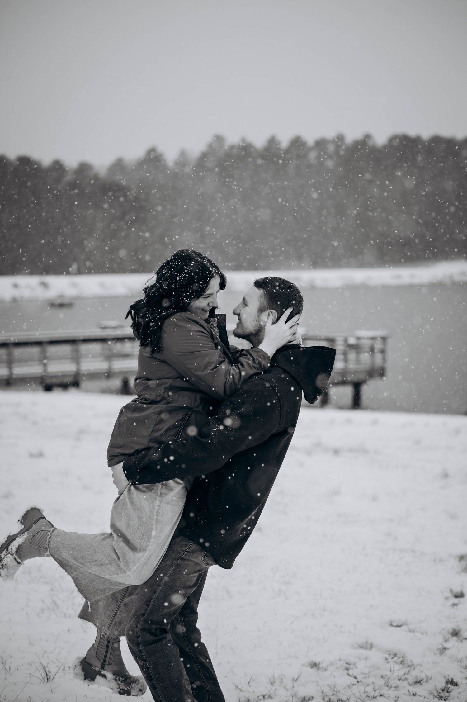 A joyful couple shares an intimate moment while dancing in the snow near a wooden fence.