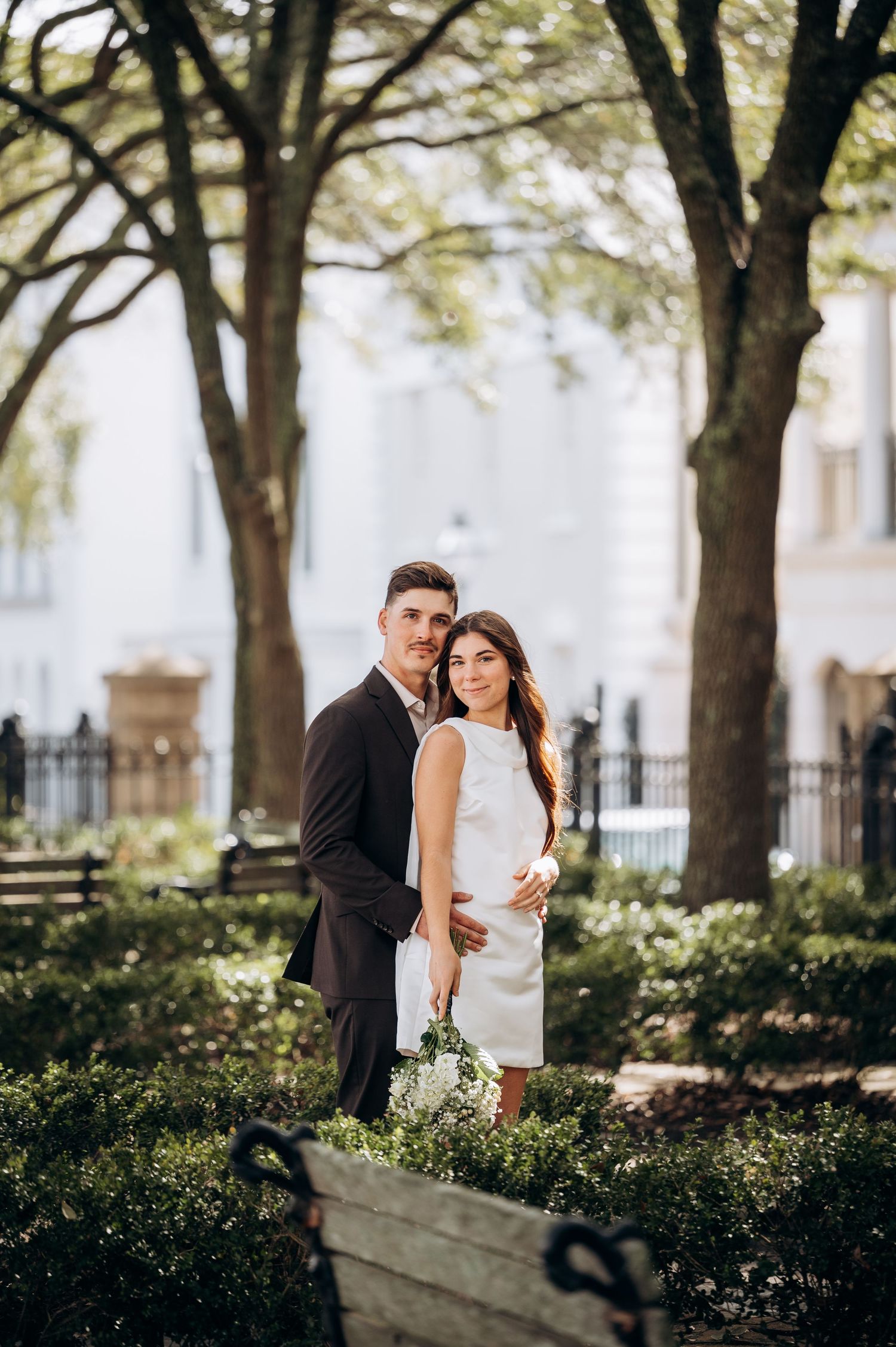 Elegant couple shares intimate moments in a garden setting with mature oak trees.