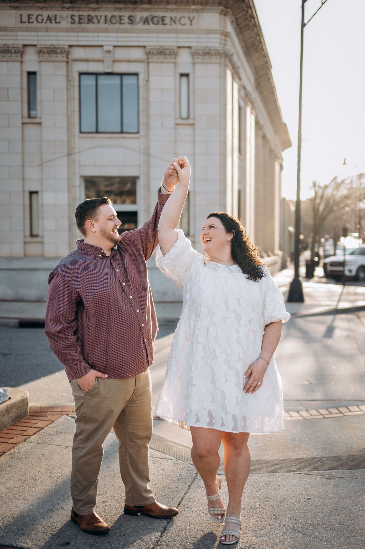 A couple dances and celebrates joyfully outside a legal services building on a sunny day.