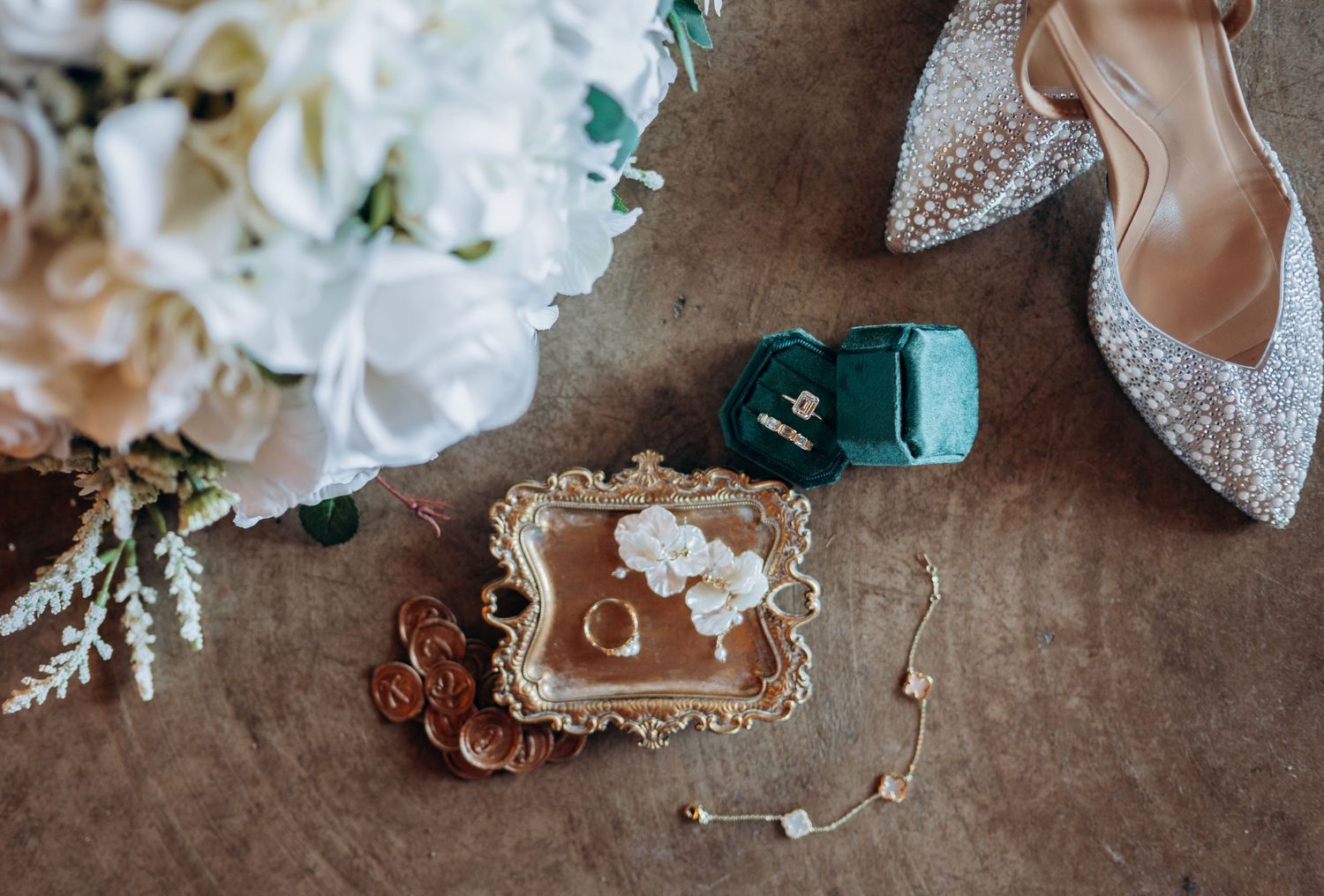 Wedding details including rings, perfume bottle, and delicate lace accessories arranged on rustic surface.