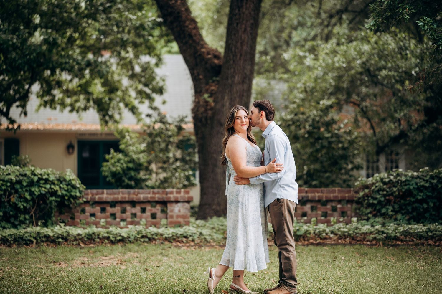 Man kissing woman on the cheek while she smiles on a lush garden lawn.