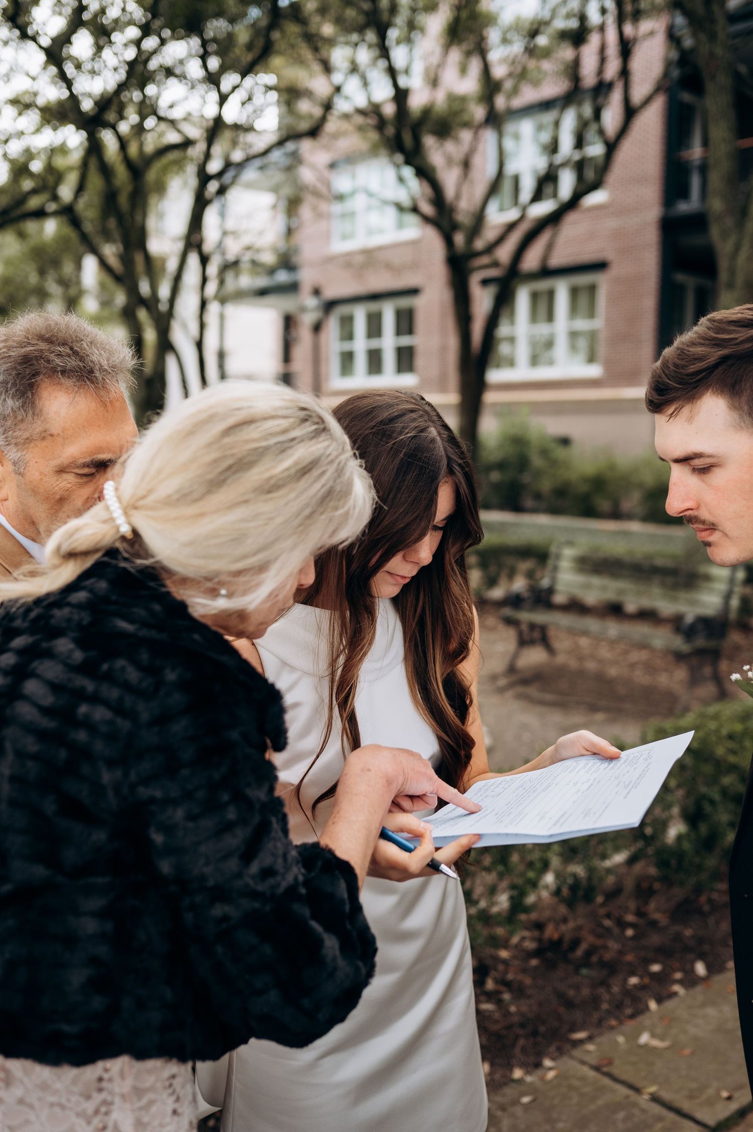 Bride, groom, and family review wedding documents outdoors after signing ceremony.