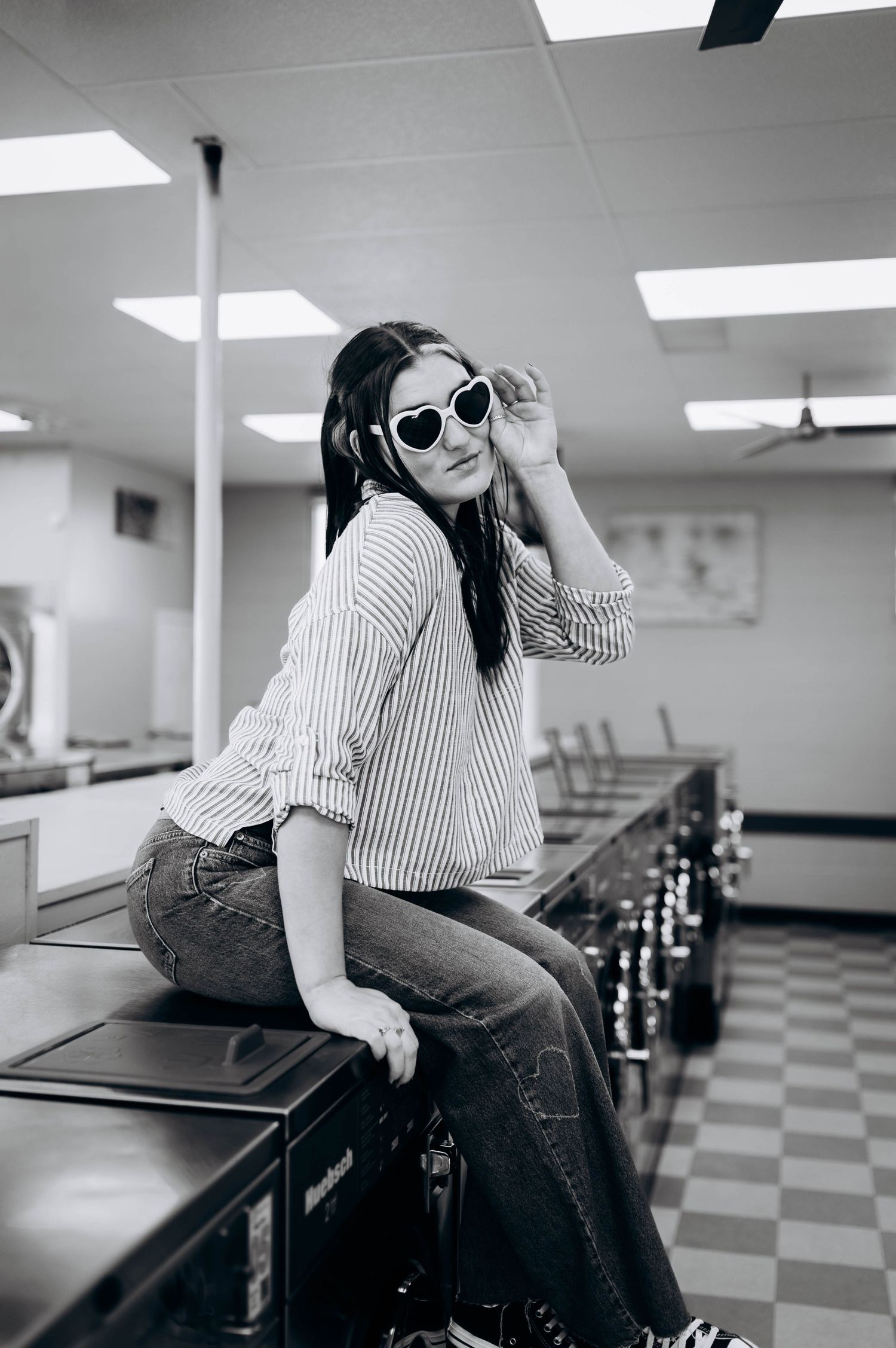 Stylish figure in striped shirt and jeans poses casually against tables in a retro-styled room with checkered floors.