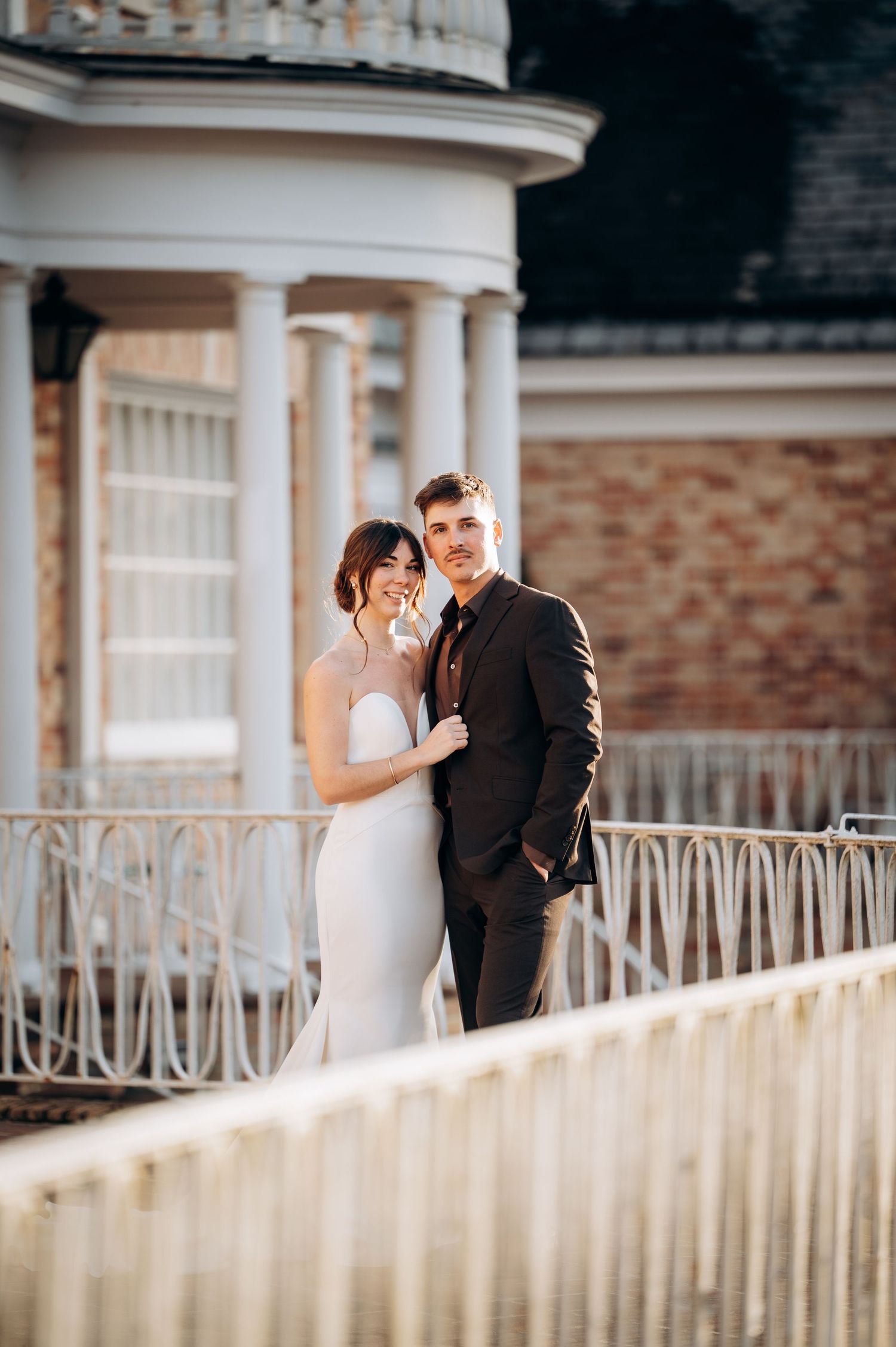 Wedding photography session along ornate white fence at elegant brick venue.
