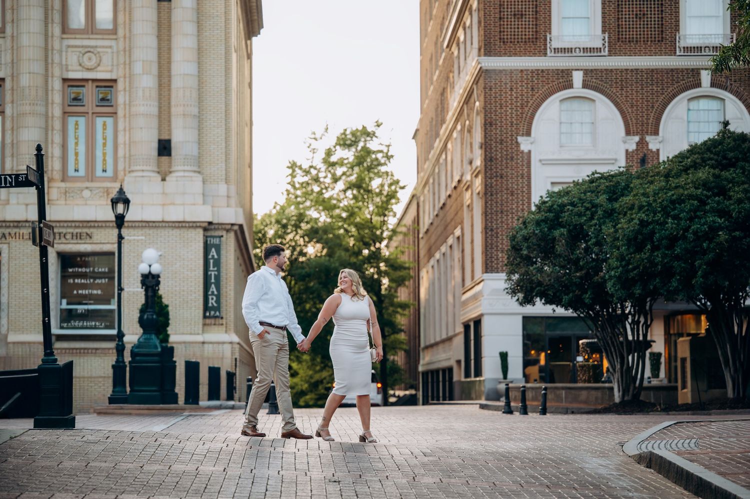A couple holds hands and walks through a charming brick downtown plaza surrounded by historic buildings.