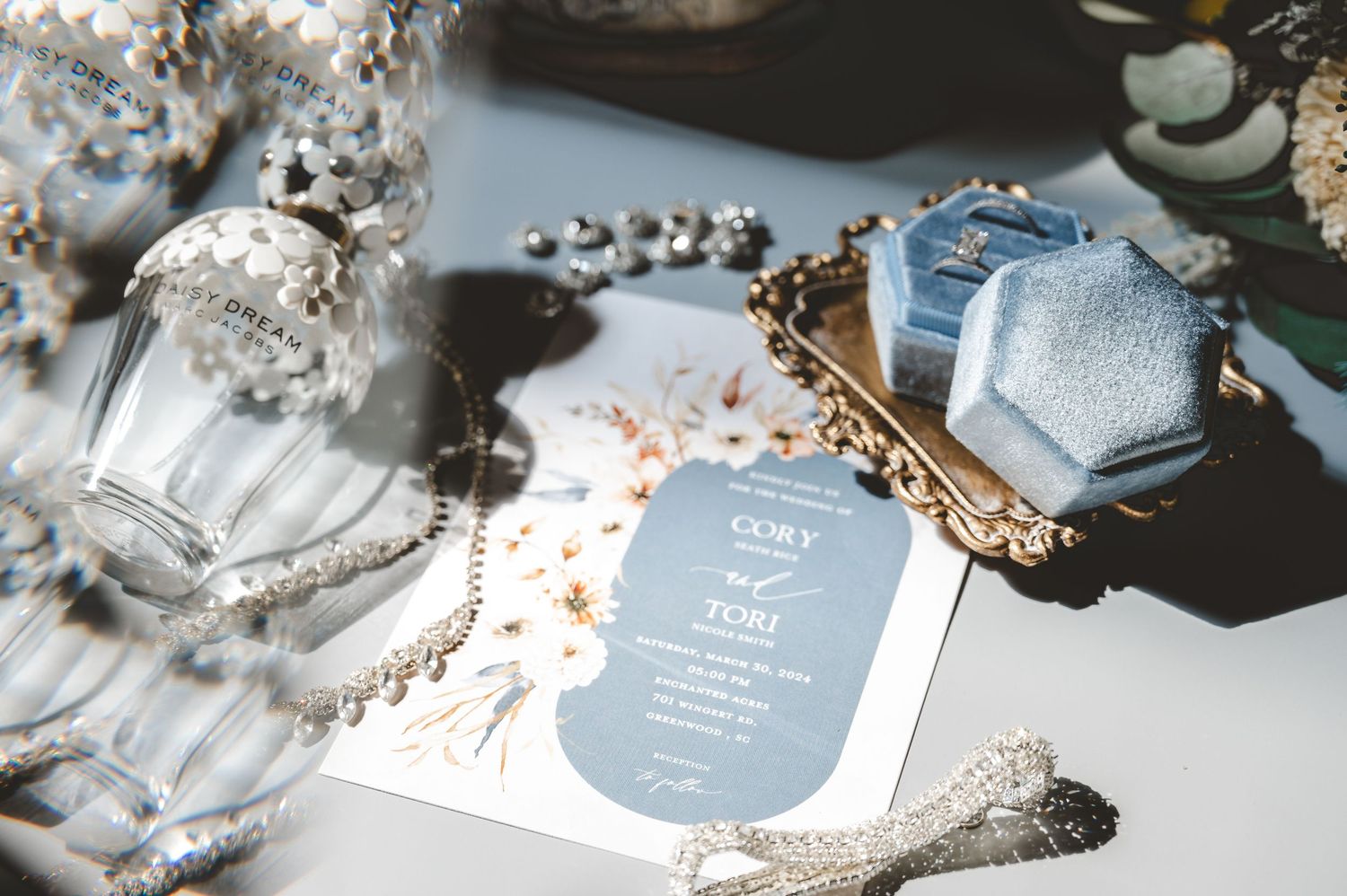 Wedding stationery and decor details in soft blue and silver tones arranged on a reflective surface.