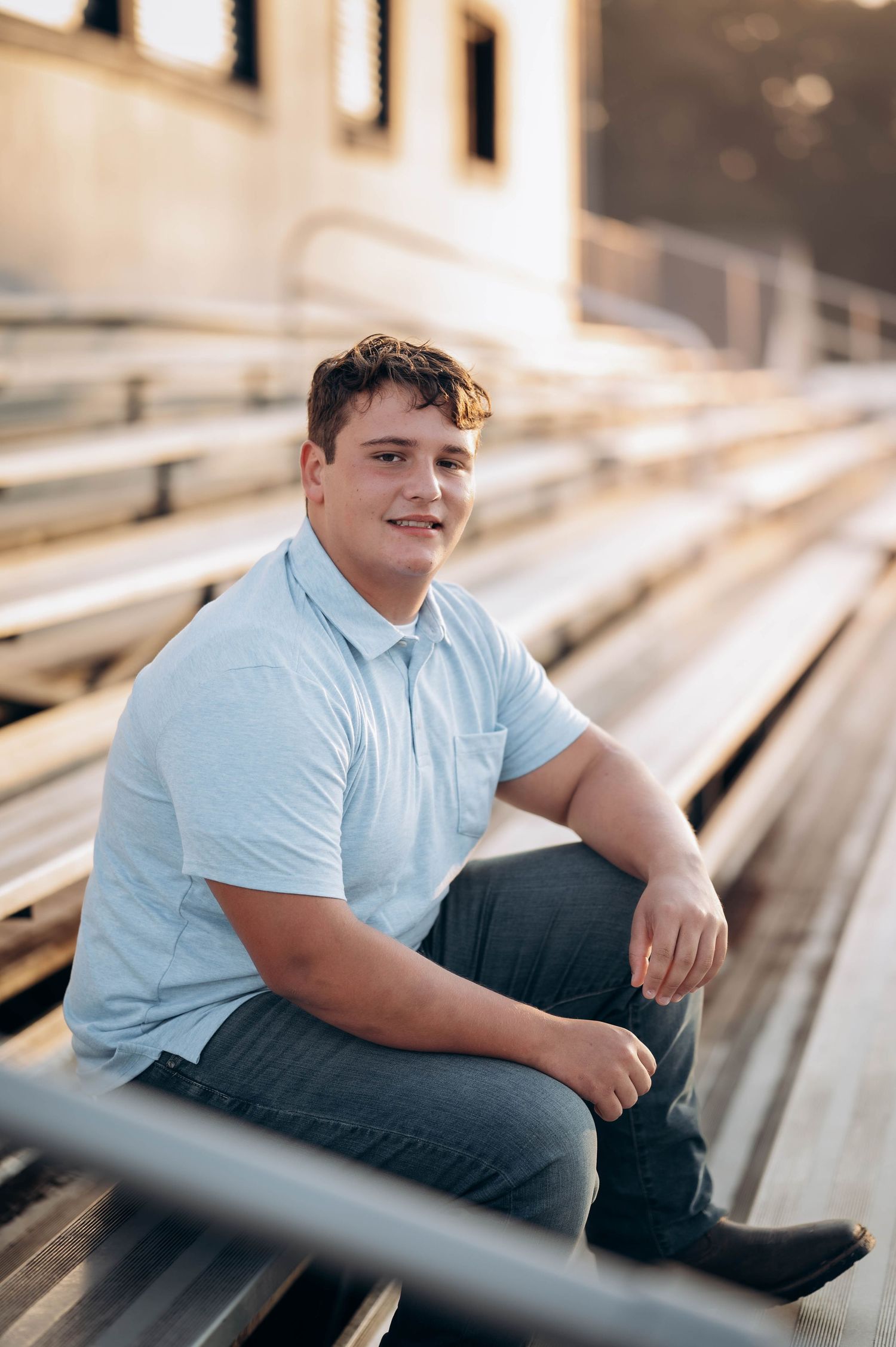 A student in light blue polo shirt sitting casually on bleacher seats.