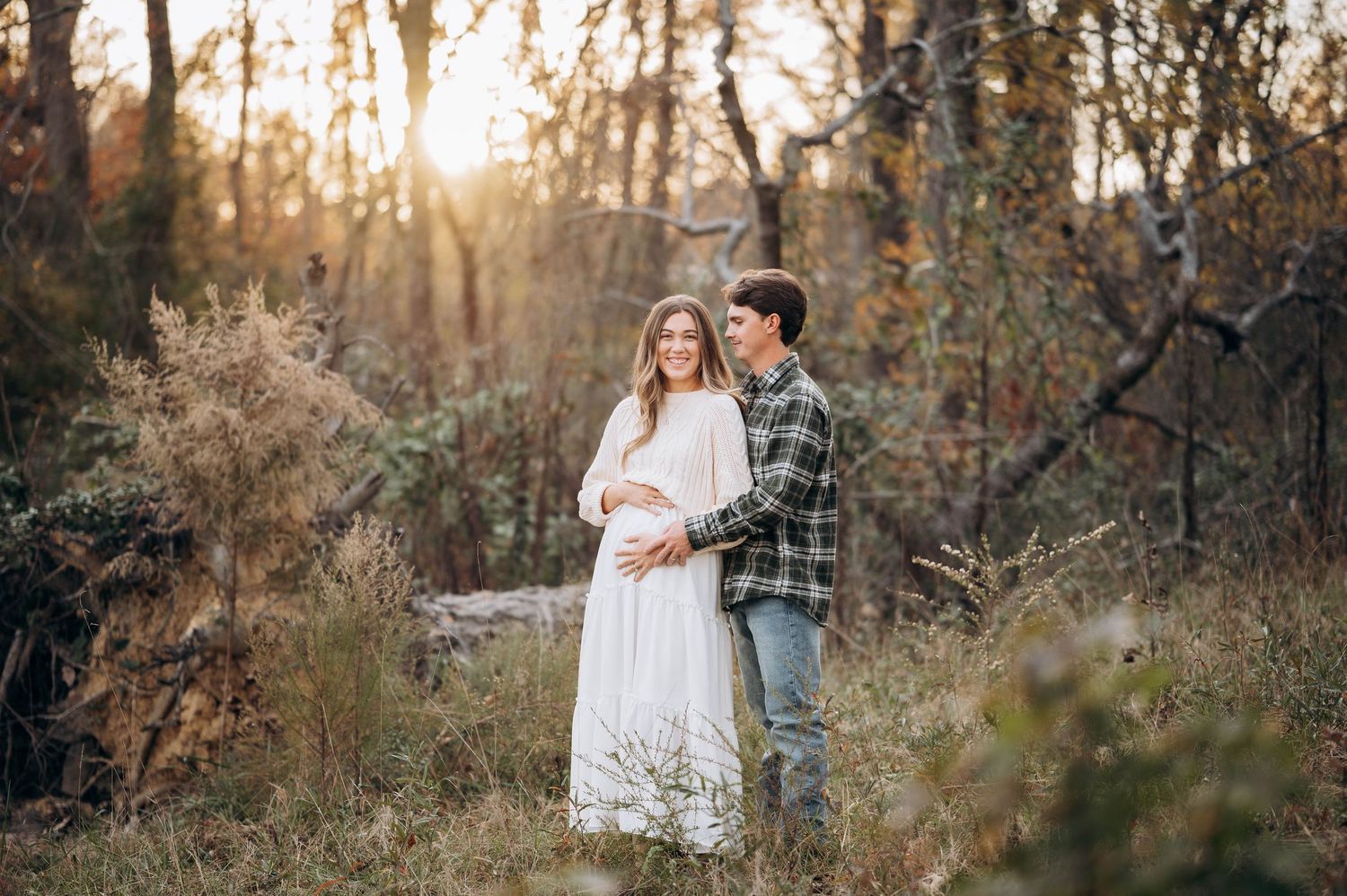 Expecting couple shares tender moment in golden sunset forest setting.