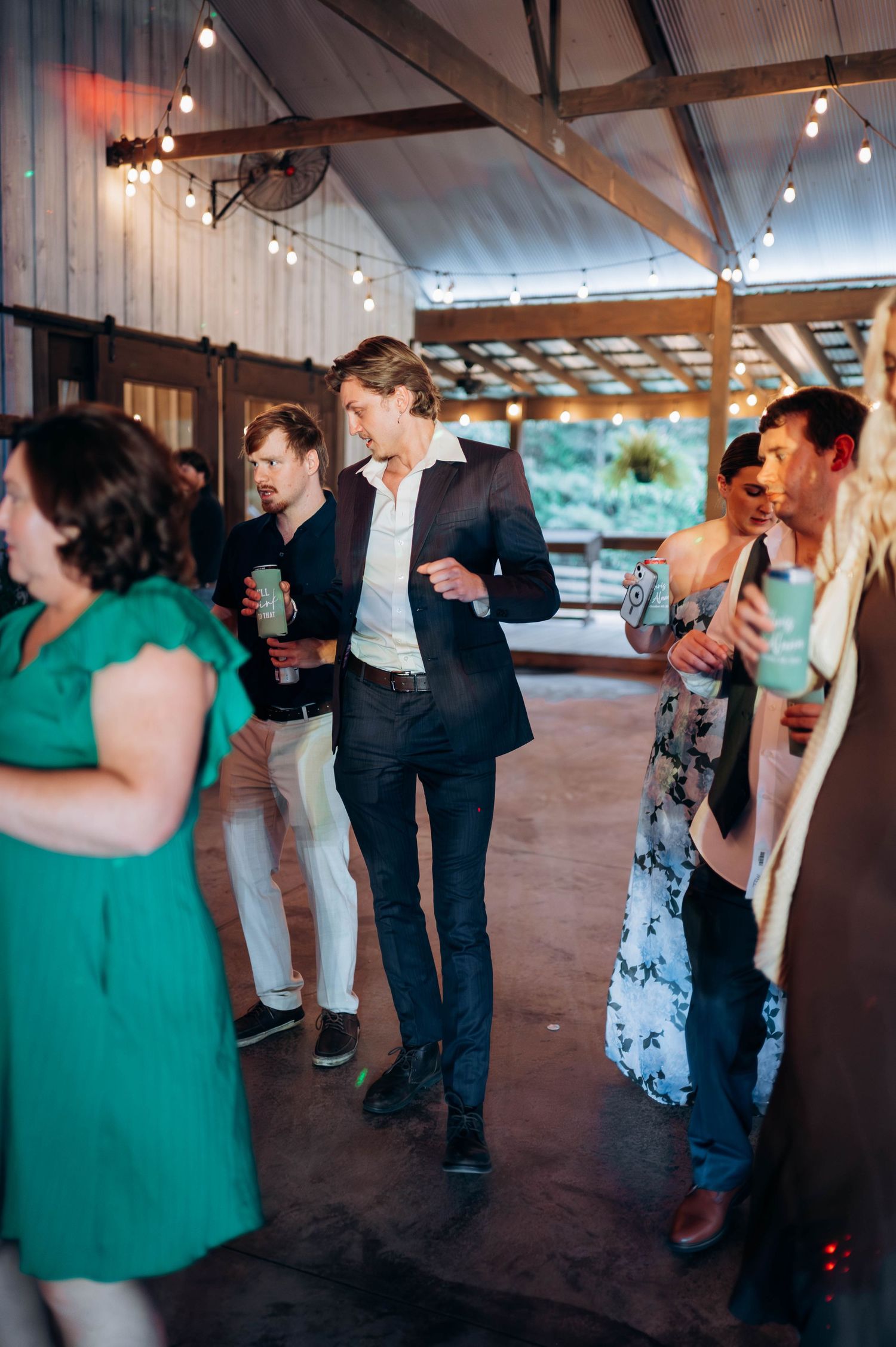 Wedding reception dance floor with guests in green and black attire under string lights.