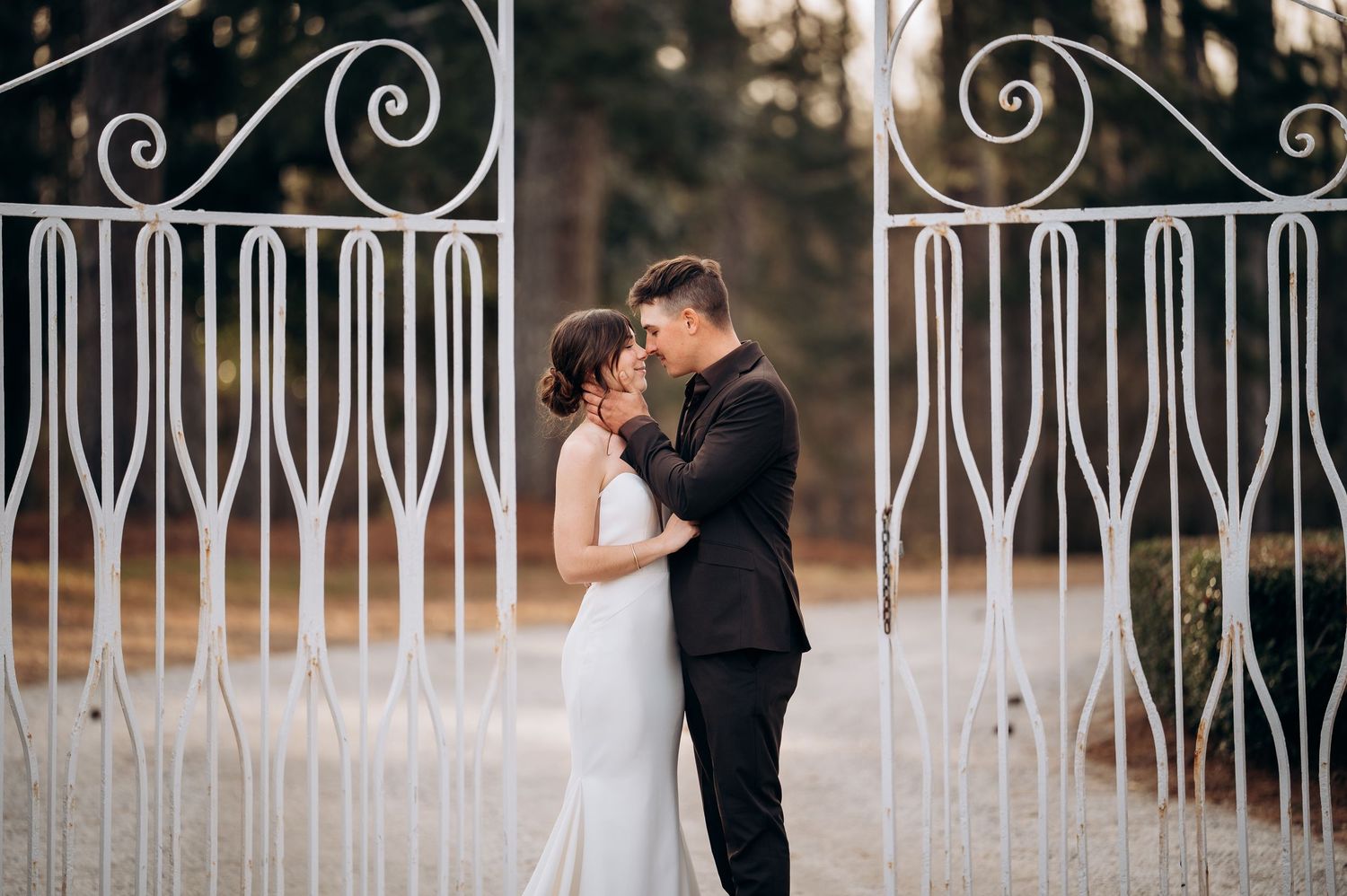 A romantic wedding photo taken through decorative white metal gates with an artistic composition.